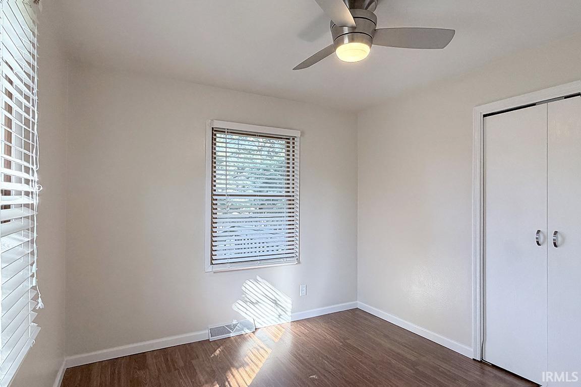 Interior room featuring wood-finish flooring, a ceiling fan with integrated lighting, and a window with blinds