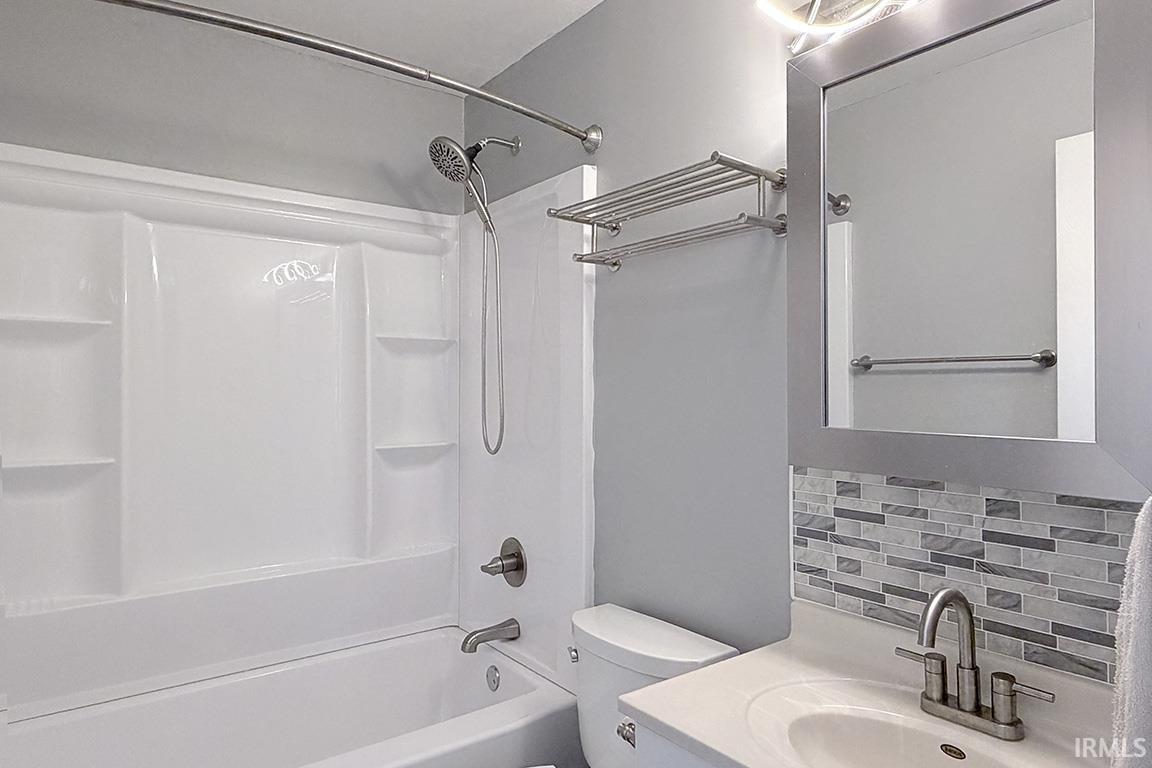 Bathroom featuring a white tub and shower combination with a curved shower rod, mosaic tile backsplash, single-sink vanity with a quartz-finish countertop, and brushed nickel fixtures
