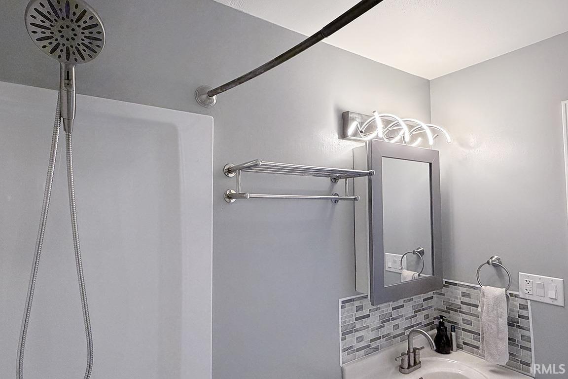Bathroom vanity featuring a mosaic tile backsplash, a rectangular mirror, and a contemporary light fixture