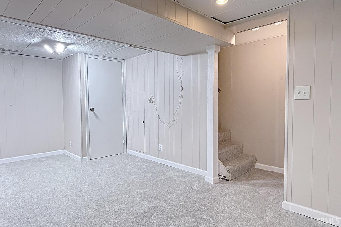 Carpeted room featuring light gray paneling, white trim, and a drop ceiling with recessed lighting