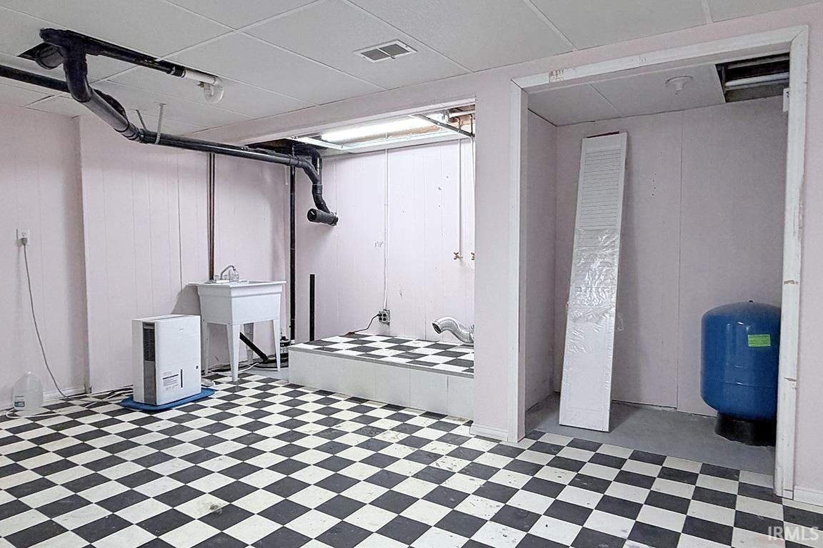 Basement area featuring a black and white checkered floor, exposed overhead piping, and a utility sink