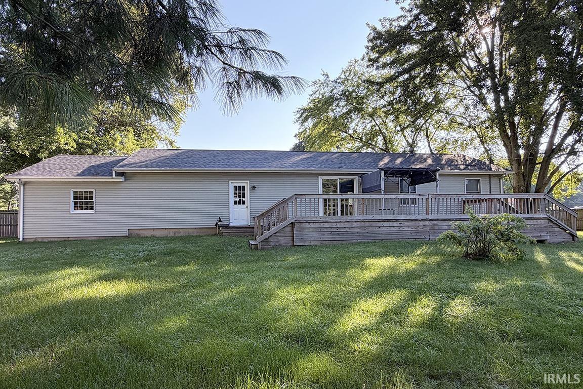 Expansive backyard featuring a large wooden deck with railings, light grey horizontal siding, a white exterior door, and a white-framed window with grilles
