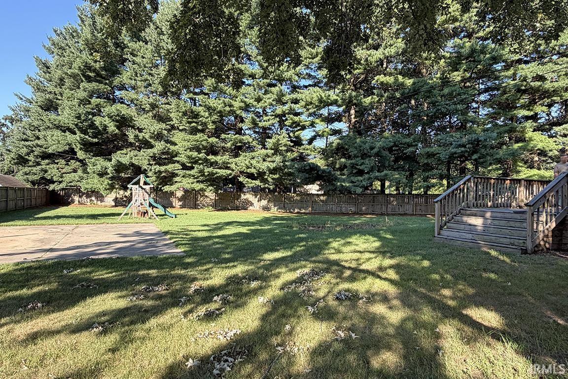 Expansive backyard with a manicured lawn, mature evergreen trees, and a wooden privacy fence