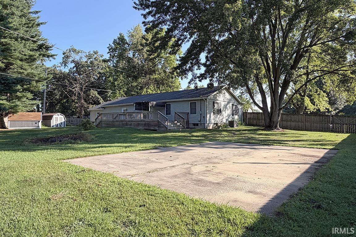 Expansive backyard with a large concrete pad, mature trees, and a privacy fence