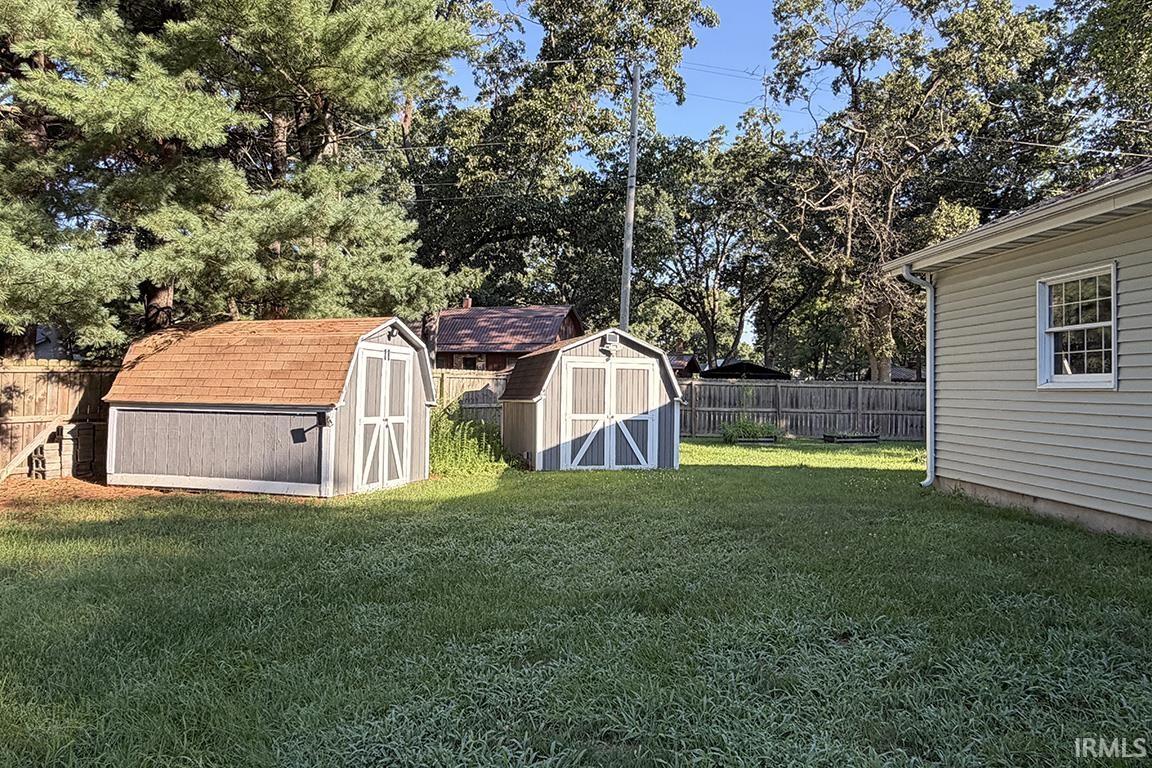 Expansive backyard featuring two utility sheds with barn-style roofs, a privacy fence, and a portion of the property's siding visible