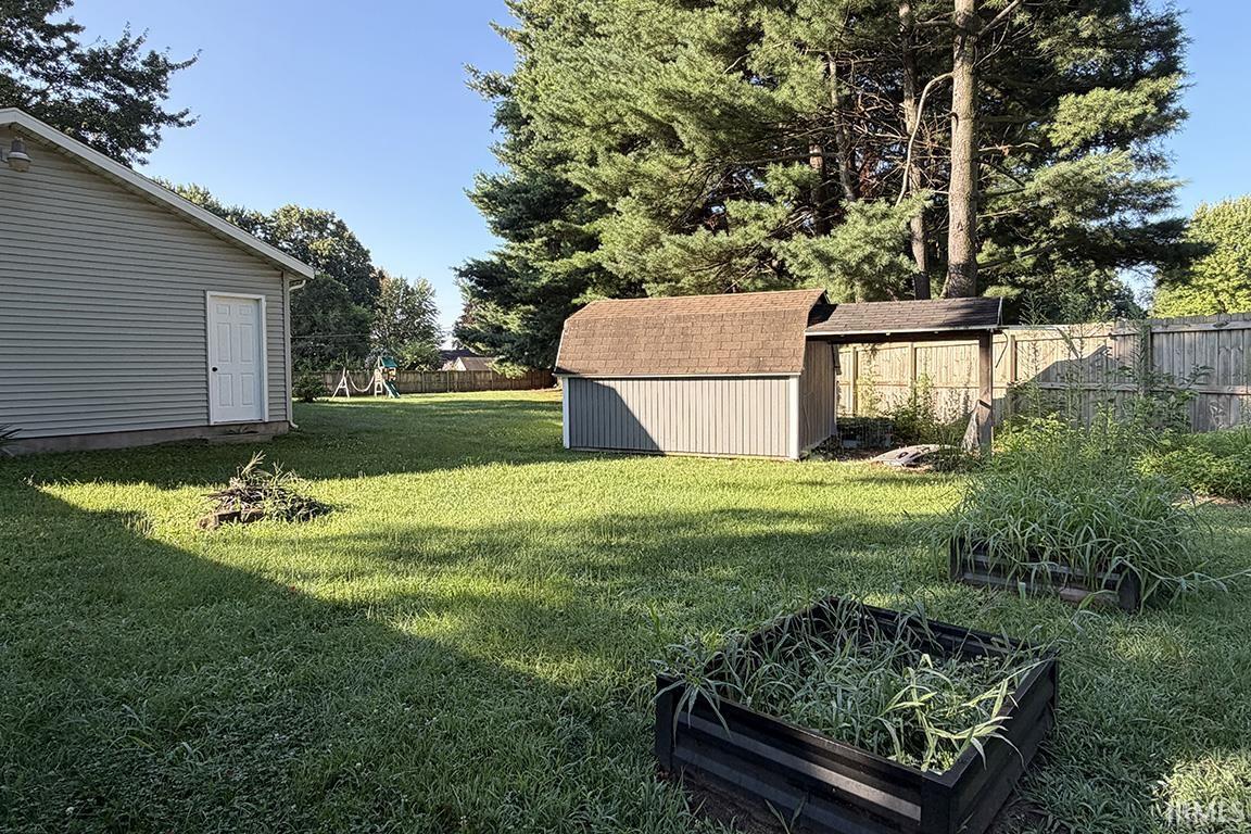 Expansive lawn area featuring a detached storage shed with a shingle roof and siding, a large wooden privacy fence, and mature evergreen trees providing natural screening