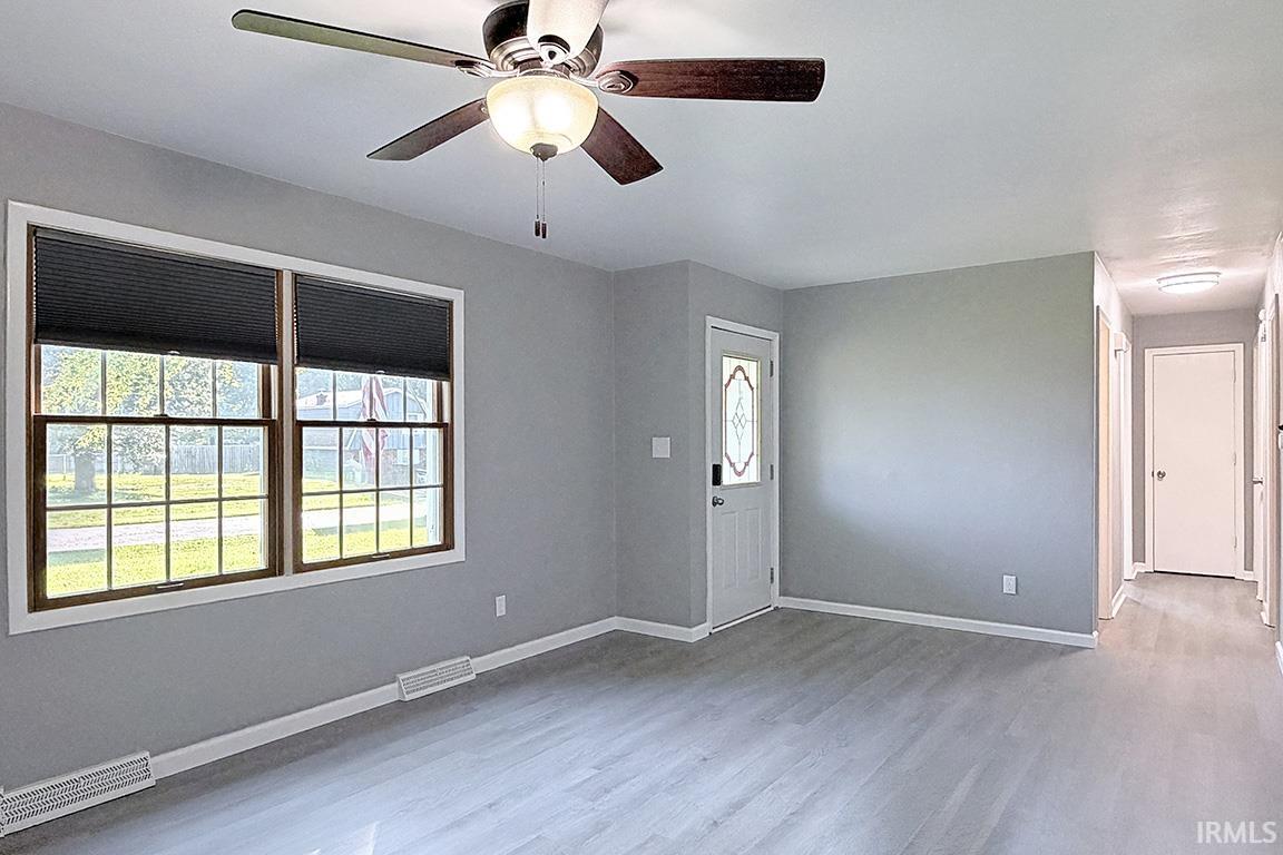 Spacious living area featuring light wood-finish flooring, neutral gray wall tones, and white trim