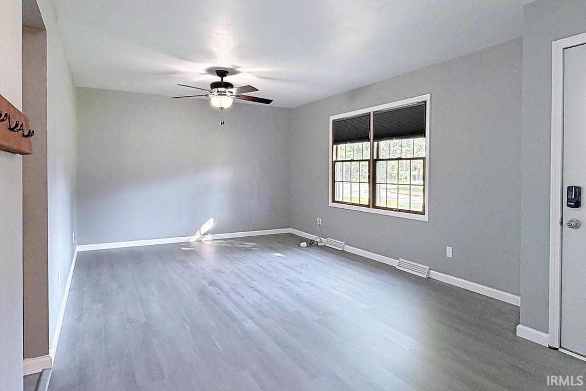 Spacious room featuring gleaming wood-finish flooring, neutral wall finishes, and abundant natural light from a large multi-pane window with cellular shades
