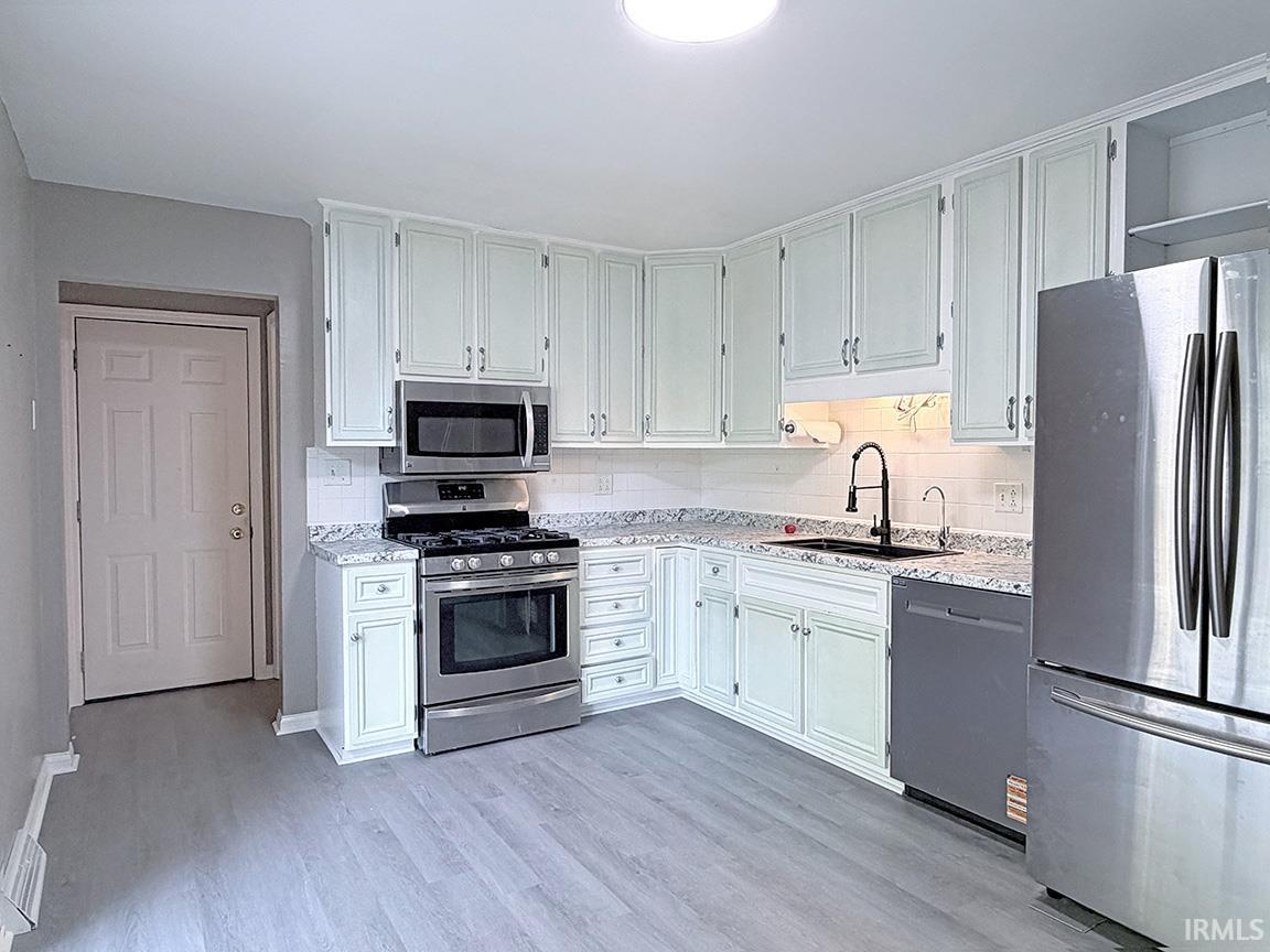 Modern kitchen featuring light-toned cabinetry, stainless steel appliances, speckled countertops, a white subway tile backsplash, and light wood-finish flooring