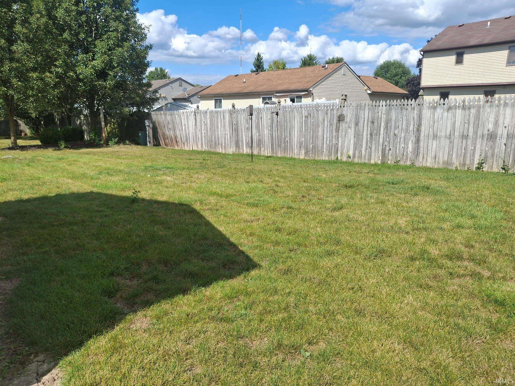 Expansive residential lot featuring a generously proportioned lawn with mature tree coverage and established wooden perimeter fencing