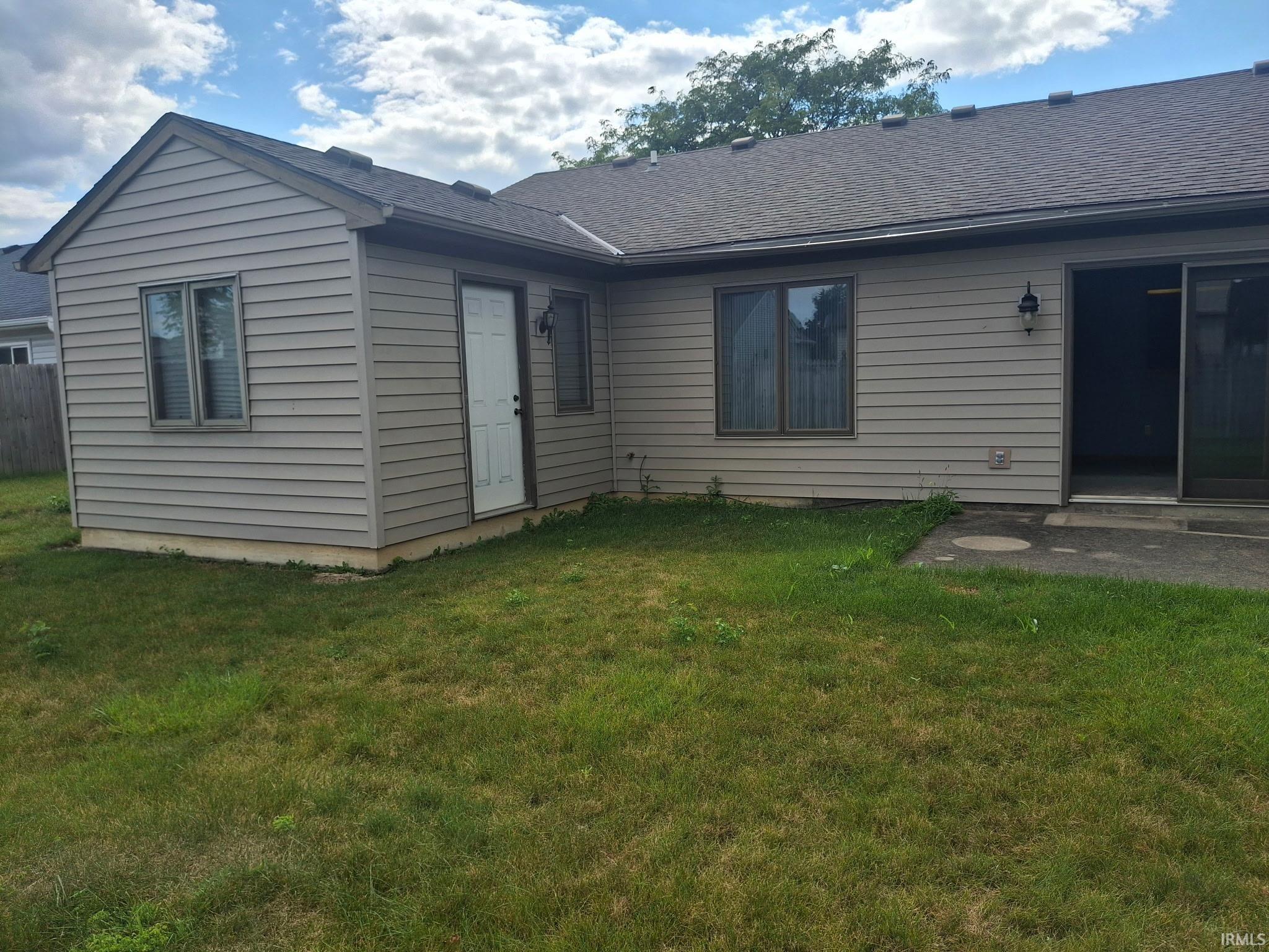 Rear exterior featuring light tan siding, a white entry door, and dark-framed windows