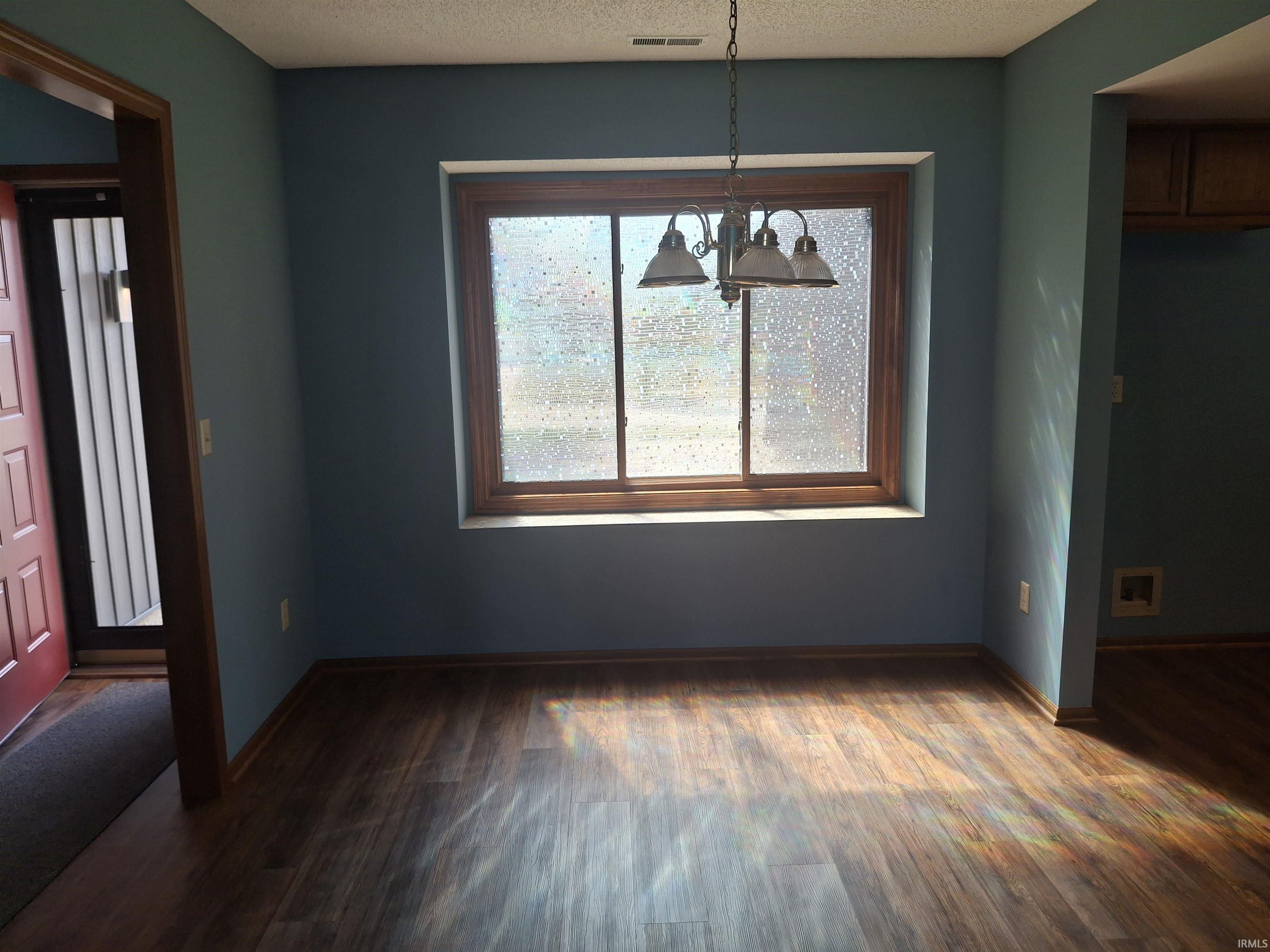 Bright corner room featuring expansive windows with natural wood framing, pendant lighting fixture, and warm wood-finish flooring throughout