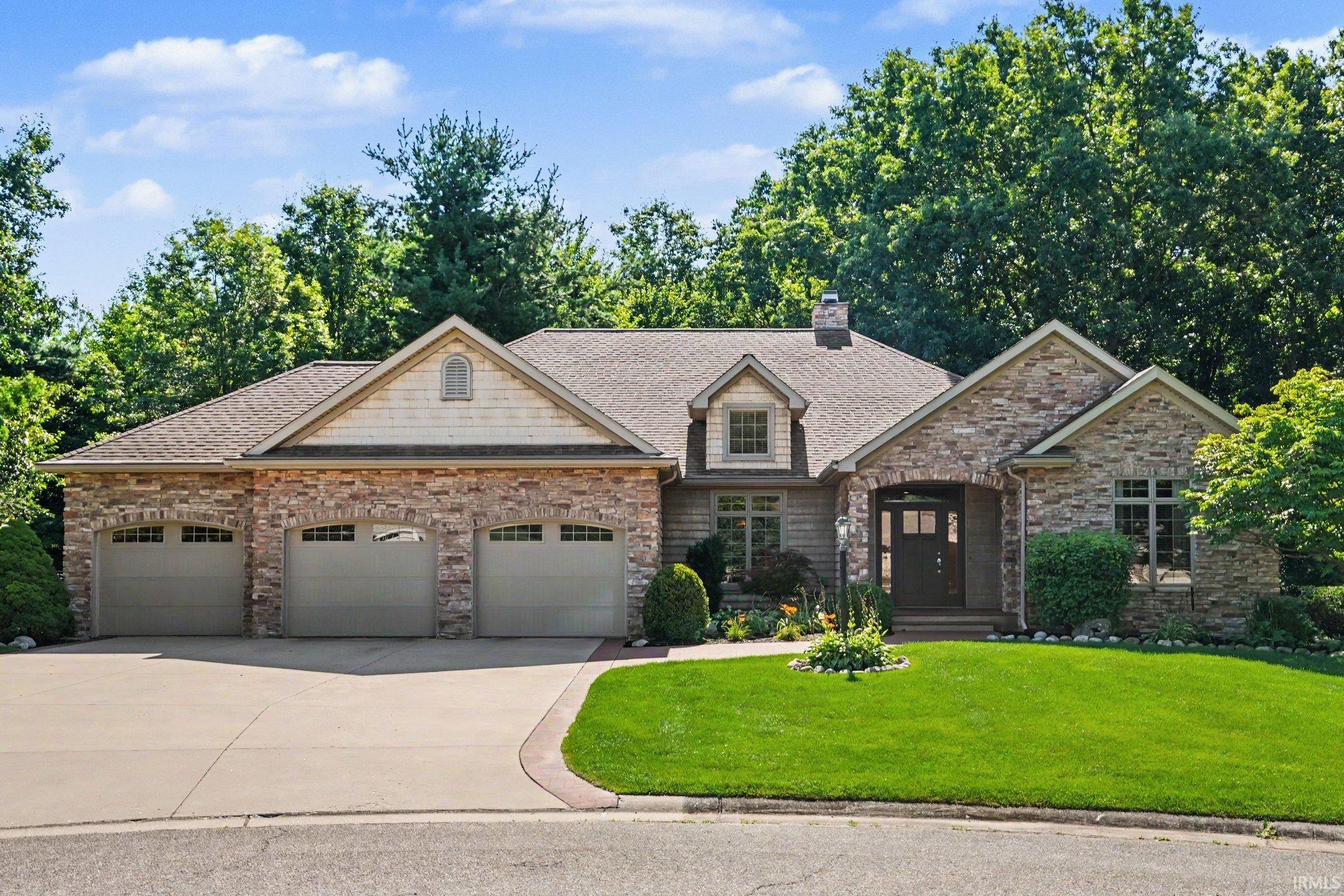 Stone and siding exterior with a three-car garage and a paved driveway