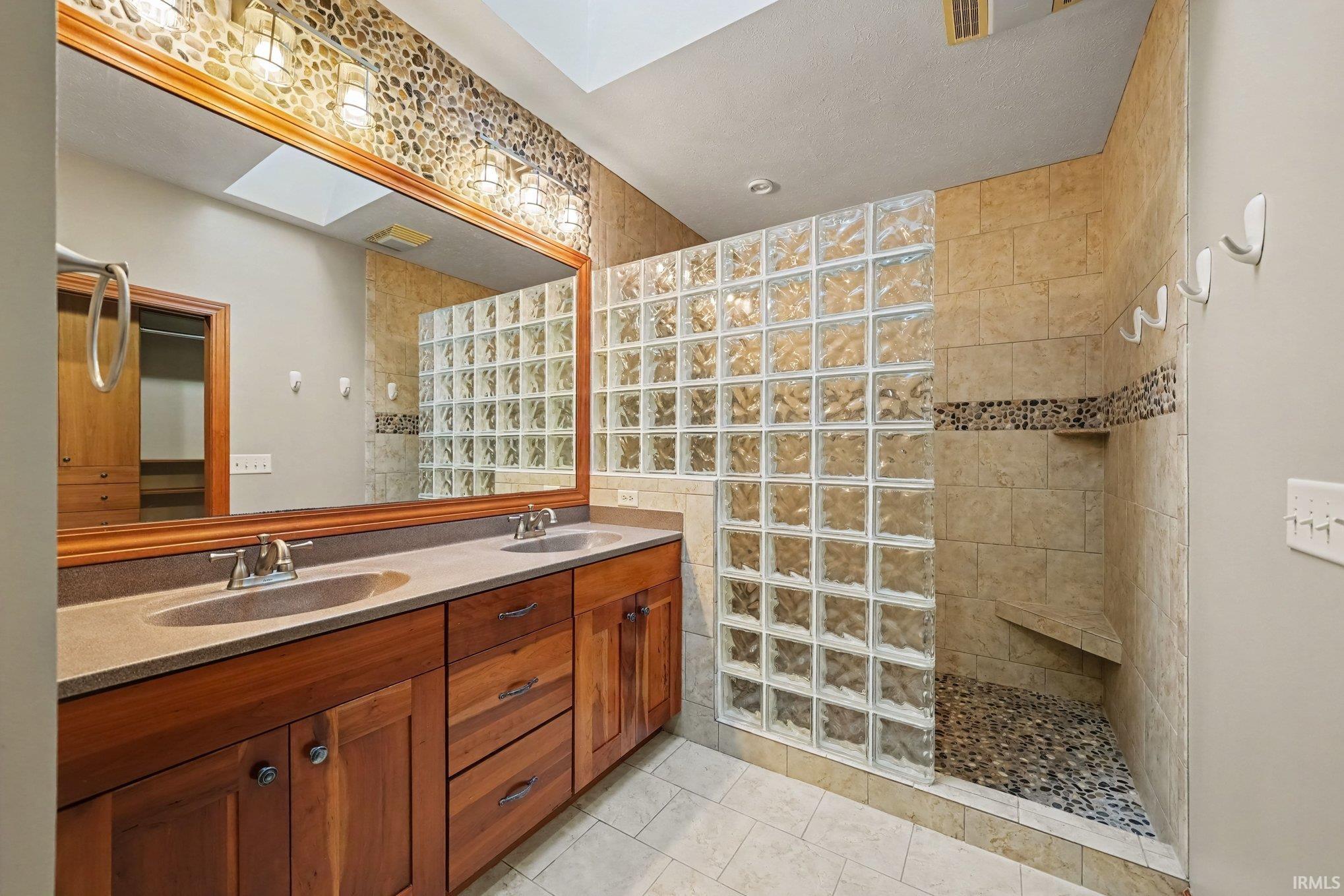 Spa-inspired bathroom featuring a custom wood vanity with dual sinks, an extensive mirror with integrated lighting and walk in Shower
