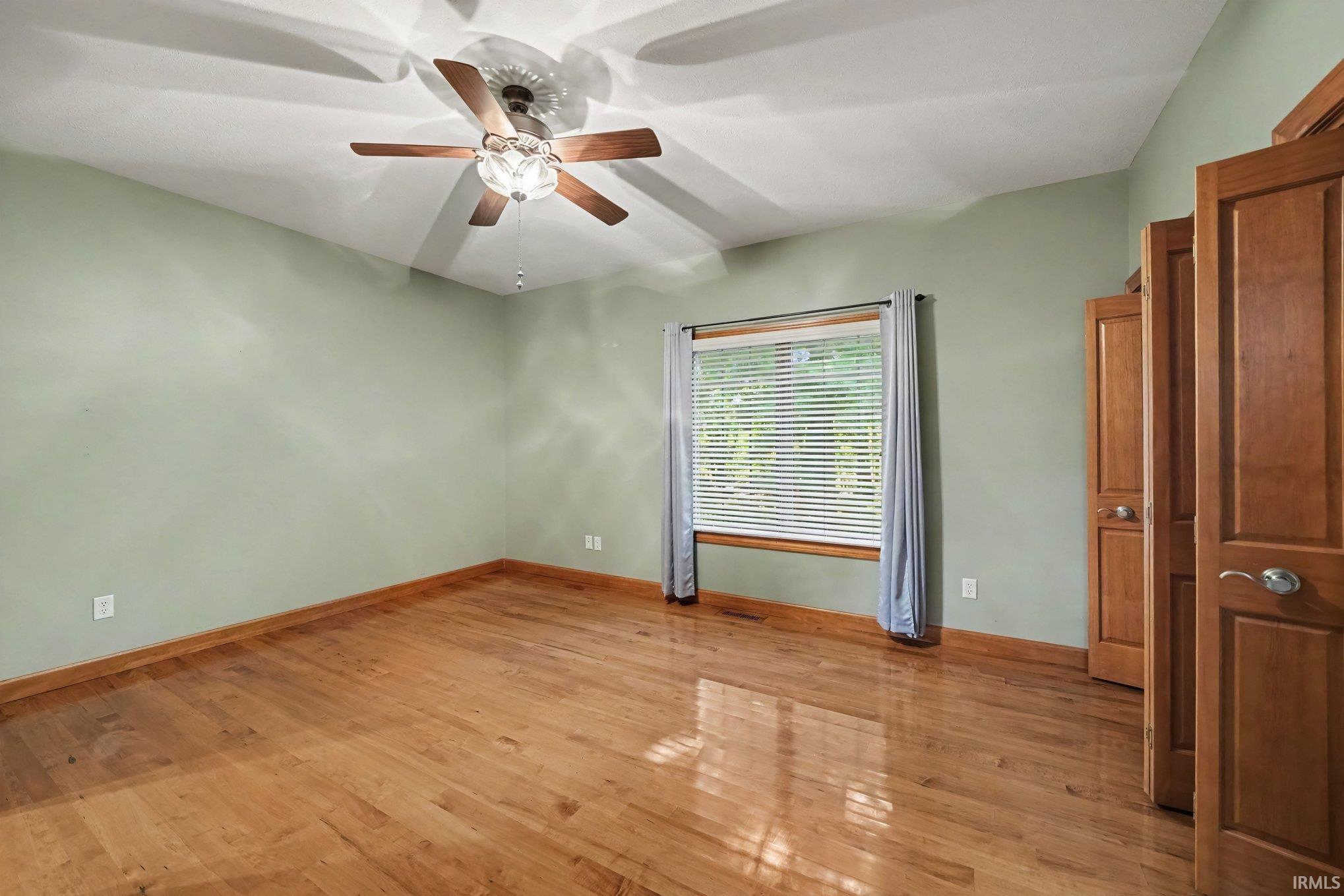 Spacious room featuring wood-finish flooring, light green walls, and a vaulted ceiling with a ceiling fan