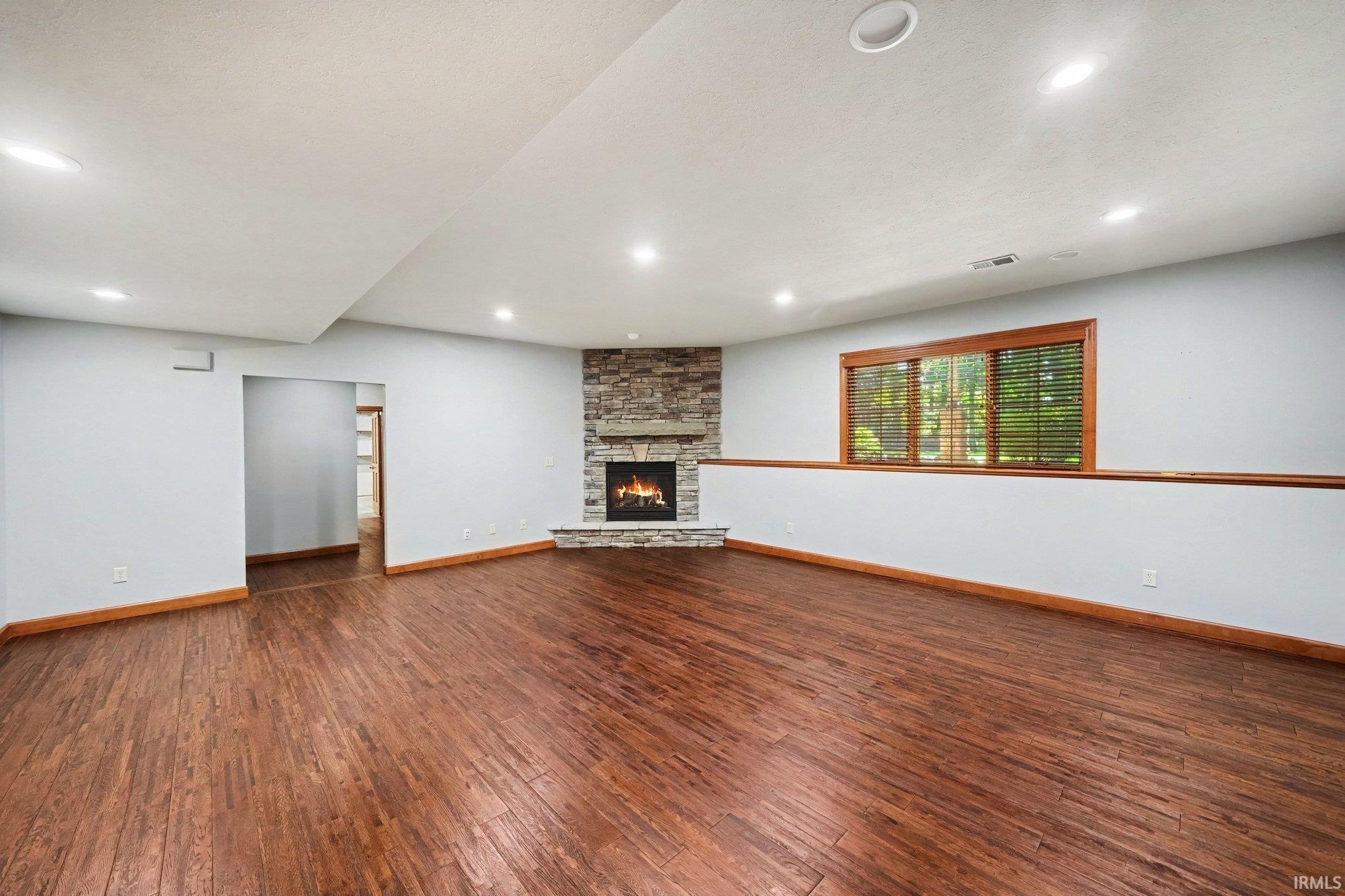 Spacious open-concept room featuring rich wood-finish flooring throughout, recessed ceiling lighting, and a gas fireplace