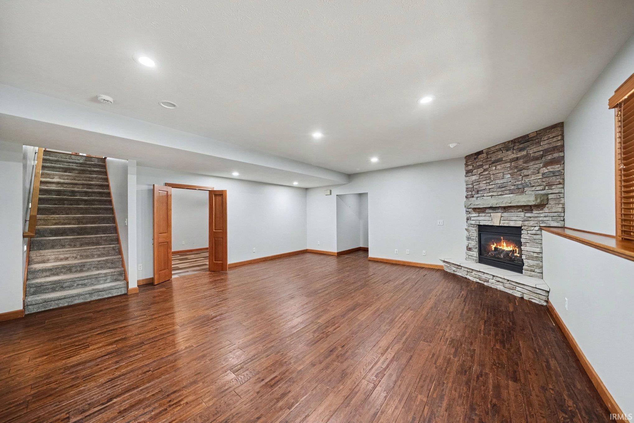 Spacious room featuring wood-finish flooring, recessed lighting, and a stone-clad fireplace with a hearth