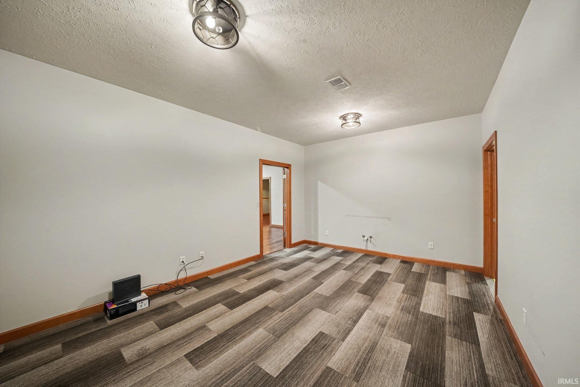 Spacious room showcasing flooring in neutral tones, recessed ceiling lighting, and pristine white walls