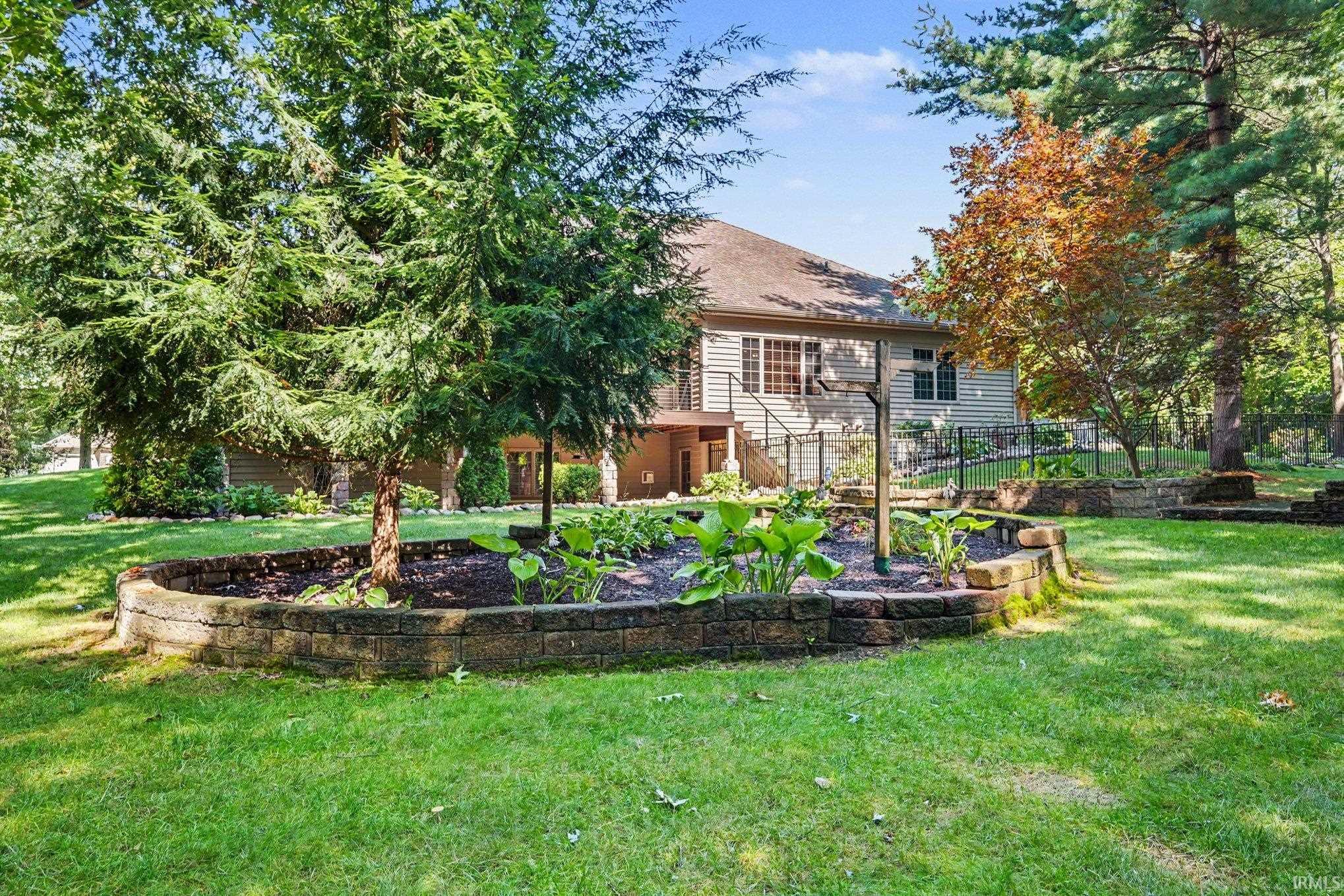 Expansive backyard featuring multiple raised garden beds with stone retaining walls, mature trees, and a manicured lawn