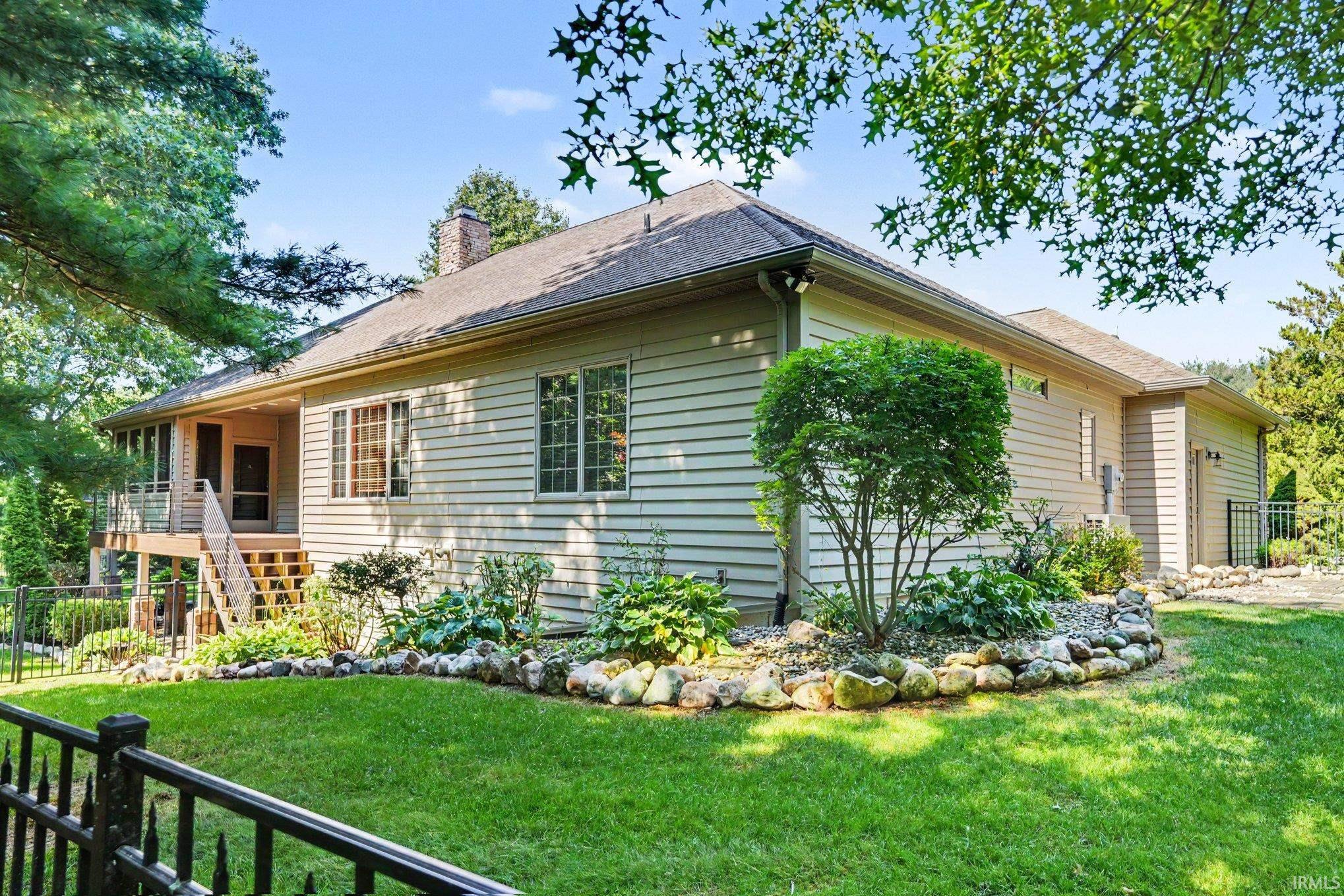 Exterior featuring neutral-toned siding, a screened-in porch with accessible stairs, a well-maintained lawn, mature landscaping with a stone border, and multiple windows with grids