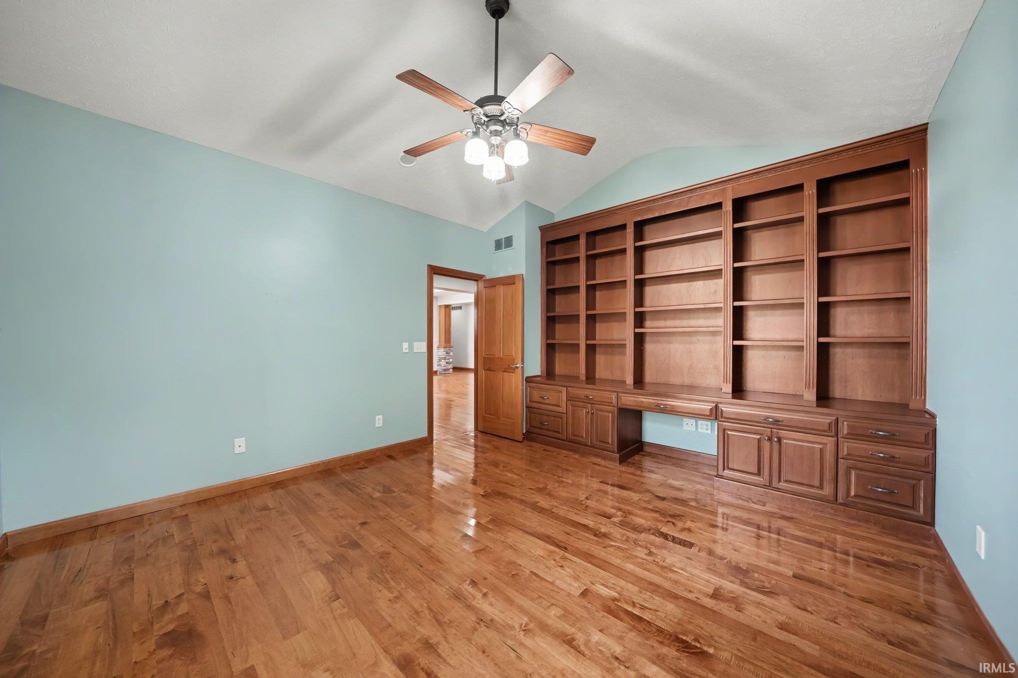 Spacious room showcasing warm wood-finish flooring, light blue walls, and a ceiling fan with integrated lighting