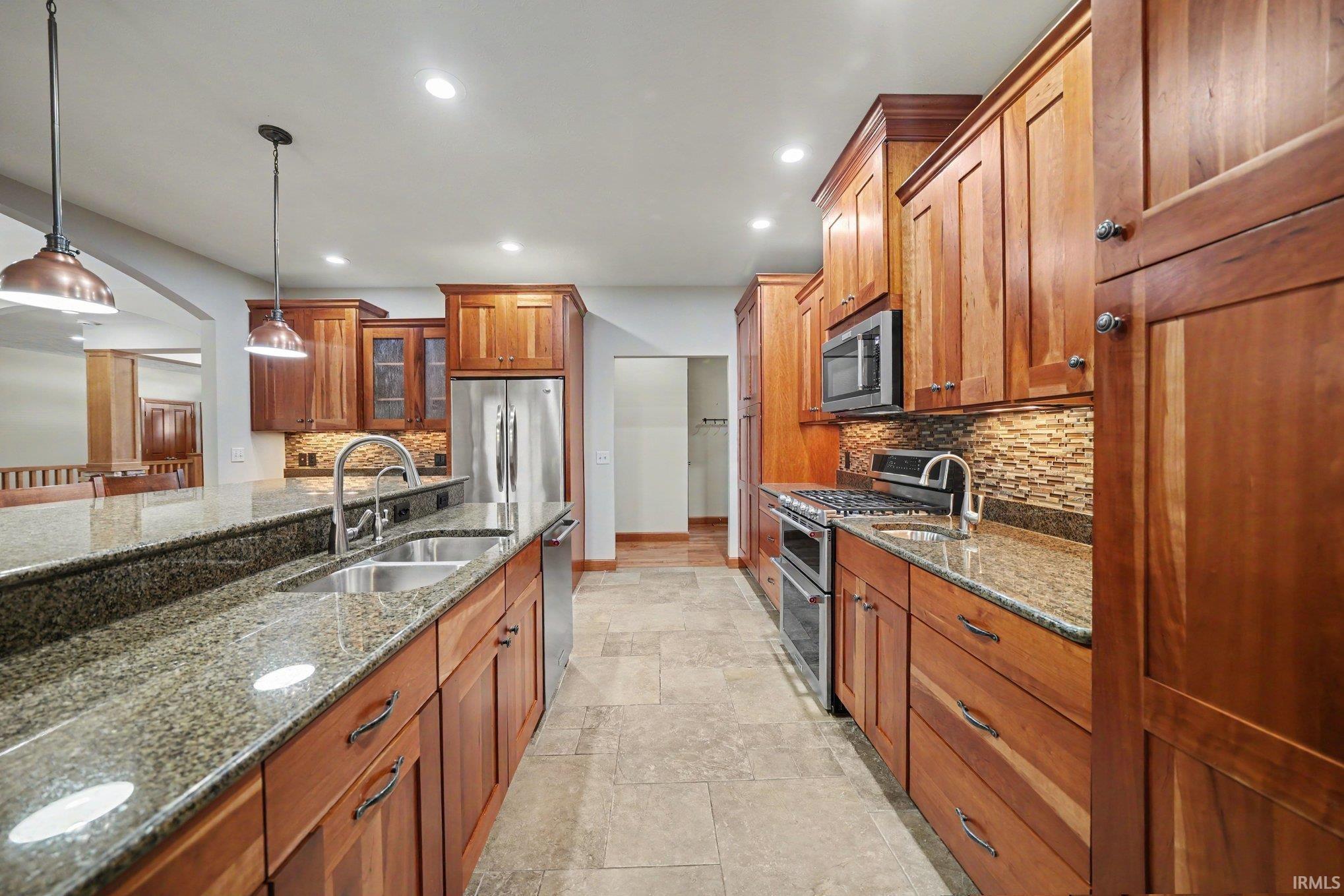 kitchen featuring rich wood cabinetry, granite countertops, stainless steel appliances including a built-in microwave and range, mosaic tile backsplash, and neutral tile flooring