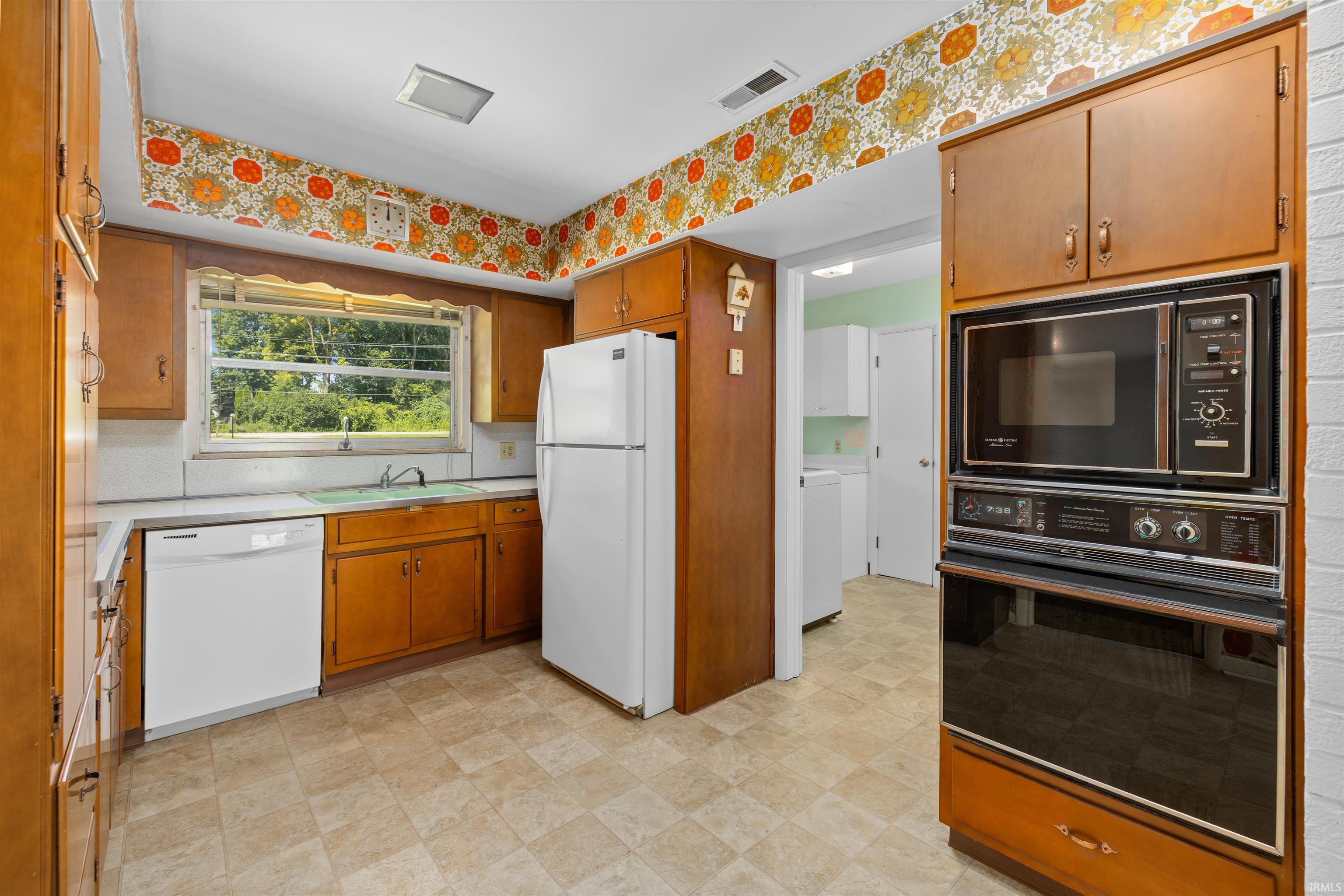 Spacious kitchen featuring wood-finish cabinetry, white appliances including a refrigerator and built-in microwave oven, tile flooring, and a window overlooking the property