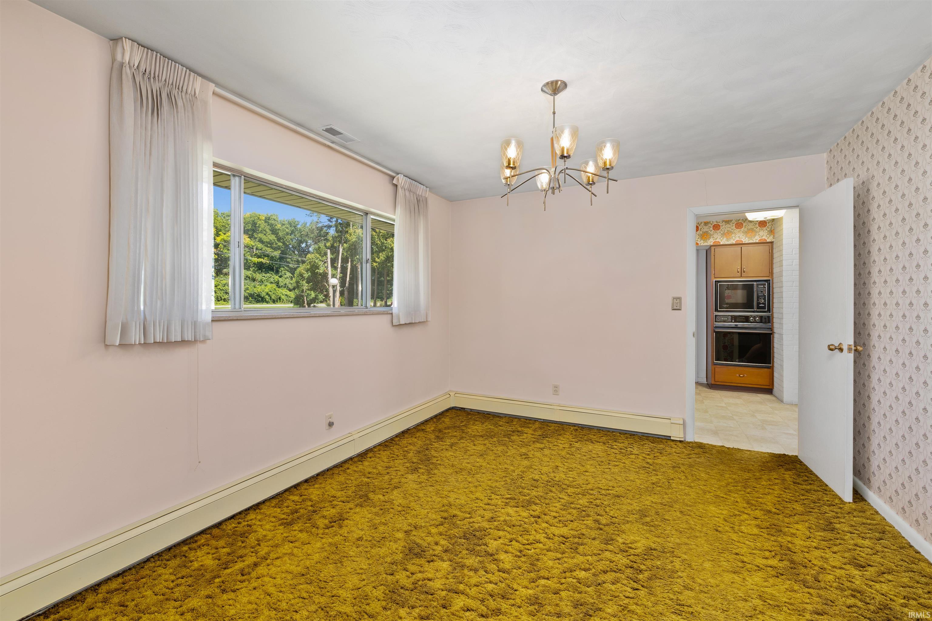 Room featuring wall-to-wall gold shag carpeting, a large window with white sheer curtains, and a contemporary chandelier