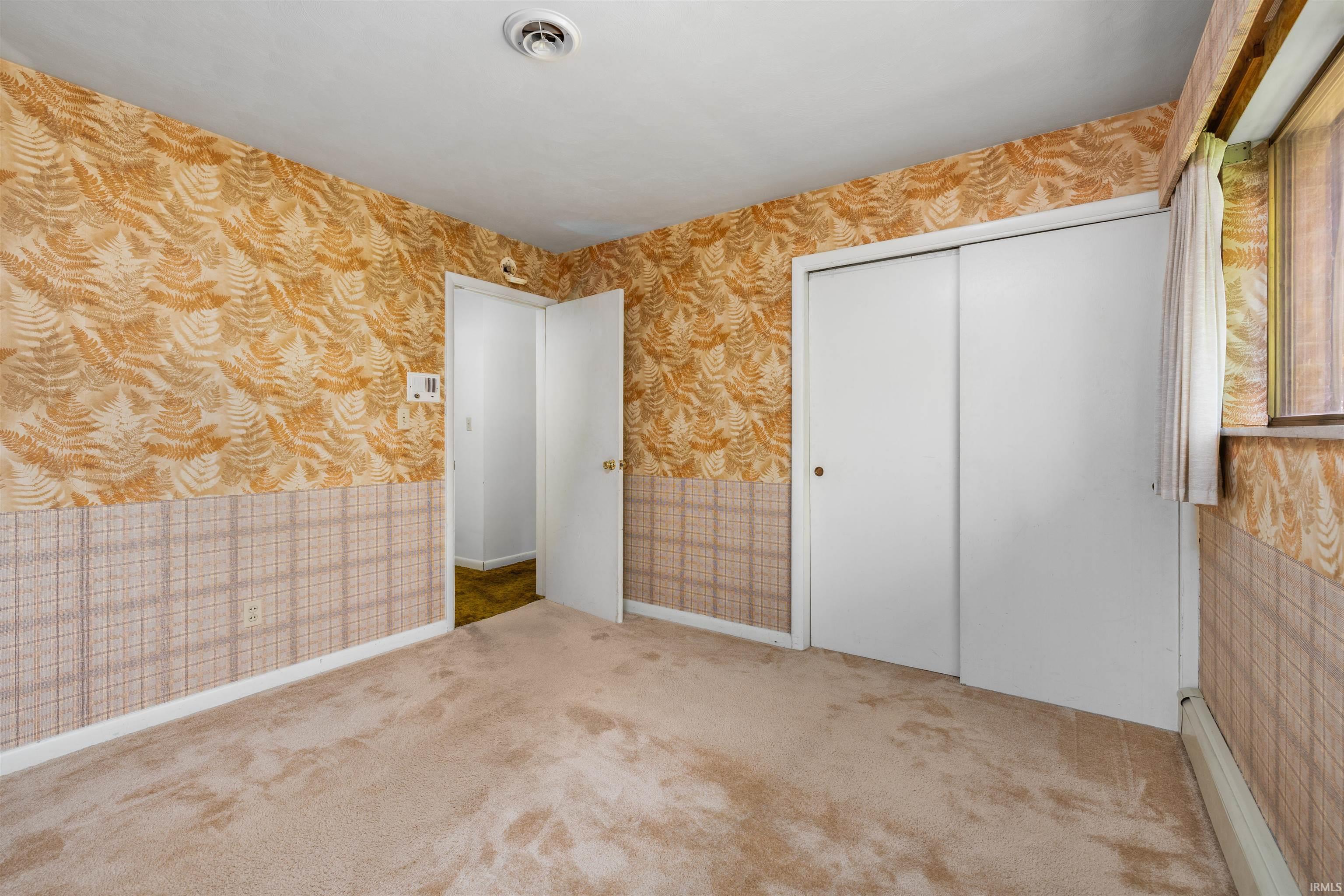 Spacious bedroom featuring ornamental patterned wallcovering on upper walls, coordinating tile wainscoting, neutral carpeting throughout, and two large closets with sliding doors providing substantial storage solutions