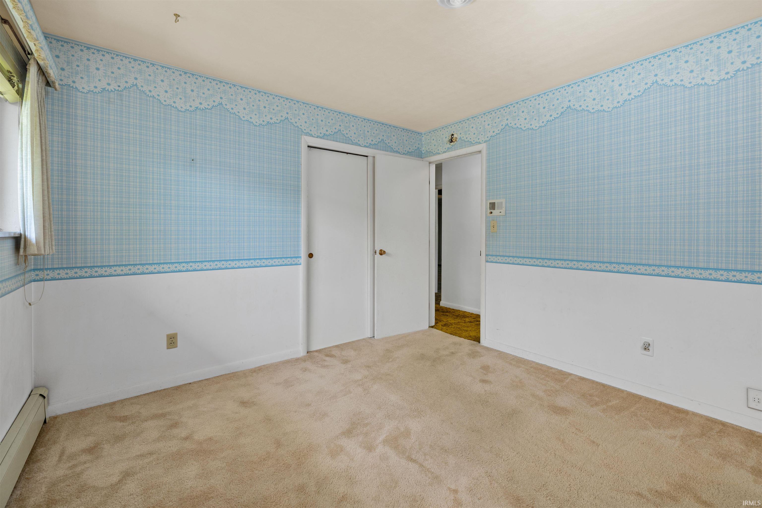 Spacious bedroom featuring soft blue and white two-tone wallcovering with coordinating border detail, neutral carpeting, and multiple closet options with white panel doors