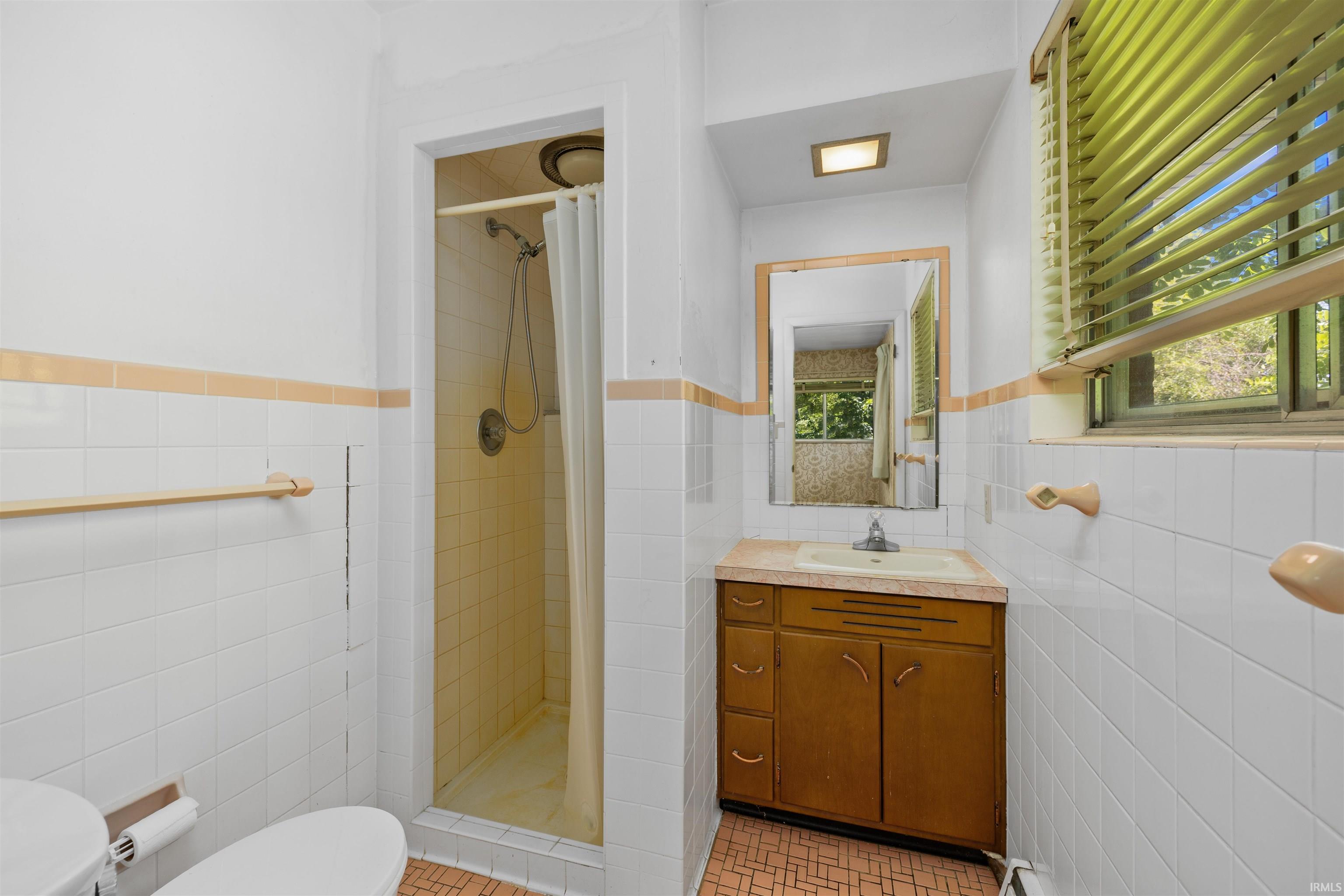 Classic bathroom featuring a wood-finish vanity with dual-sink storage, ceramic tile walls with contrasting horizontal stripe detailing, and a separate shower enclosure with glass door