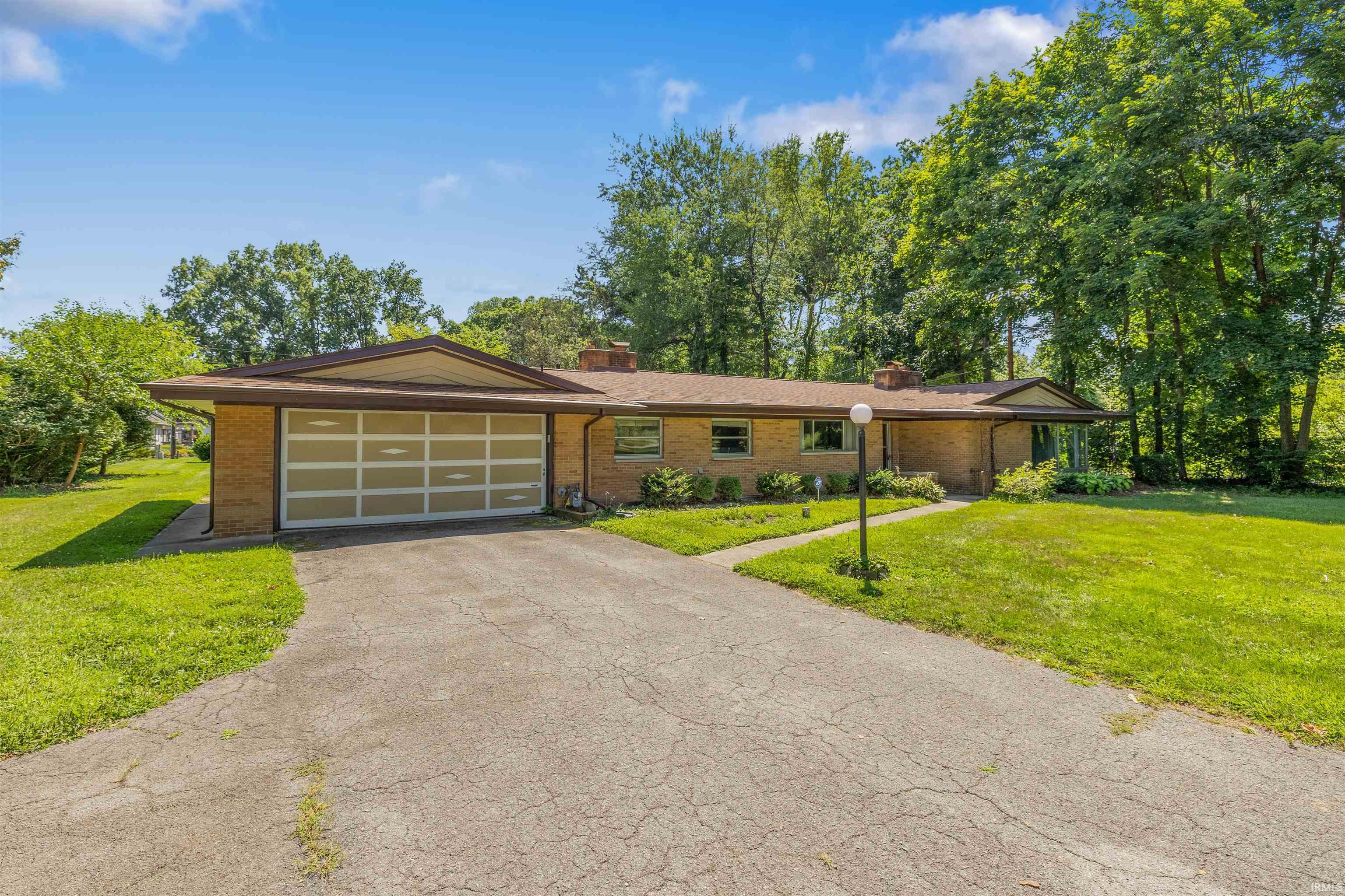 Brick ranch home featuring a modern metal-frame garage door, concrete driveway, and mature landscaping with established trees
