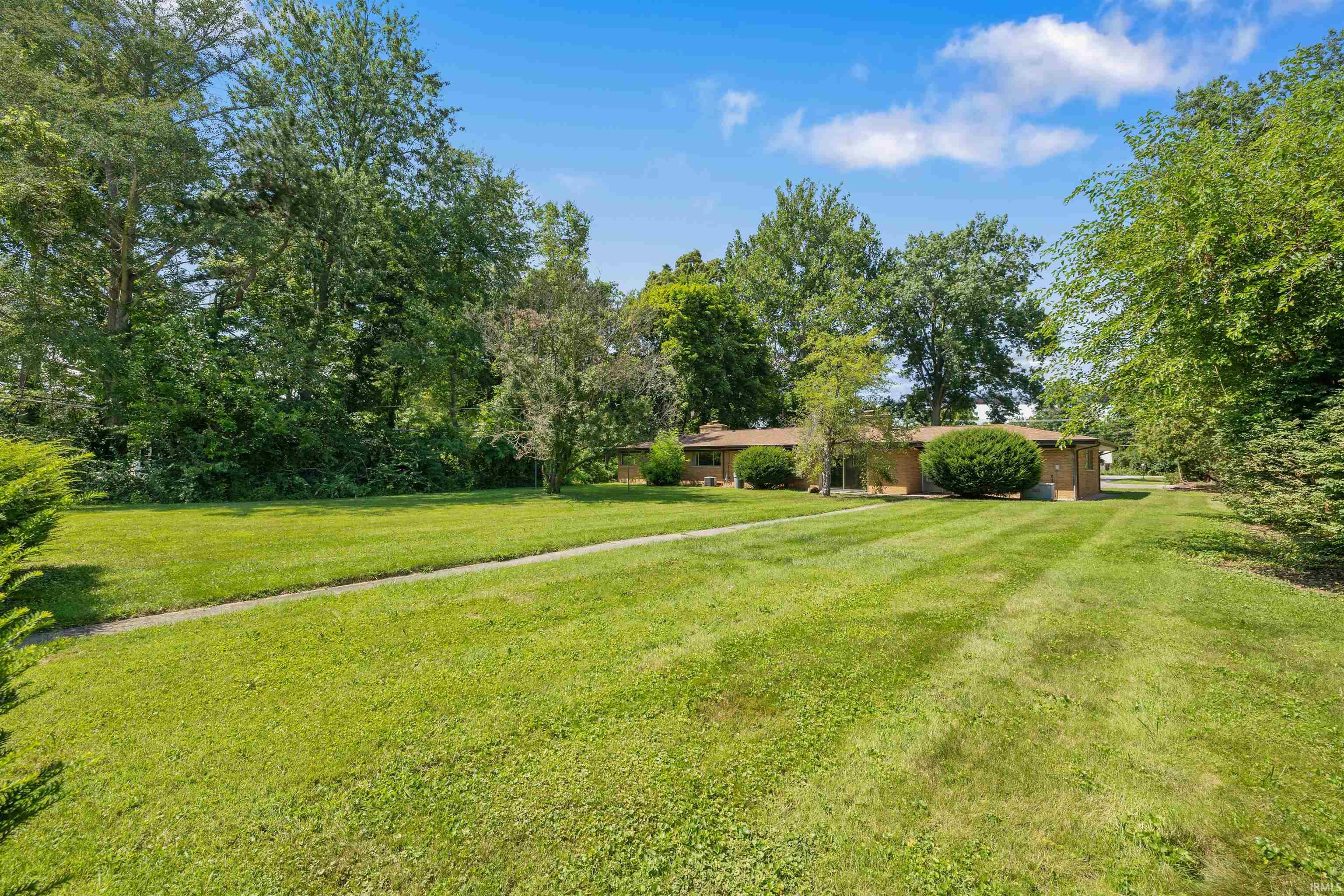 Expansive manicured lawn with mature tree-lined perimeter and brick architectural elements visible in the distance