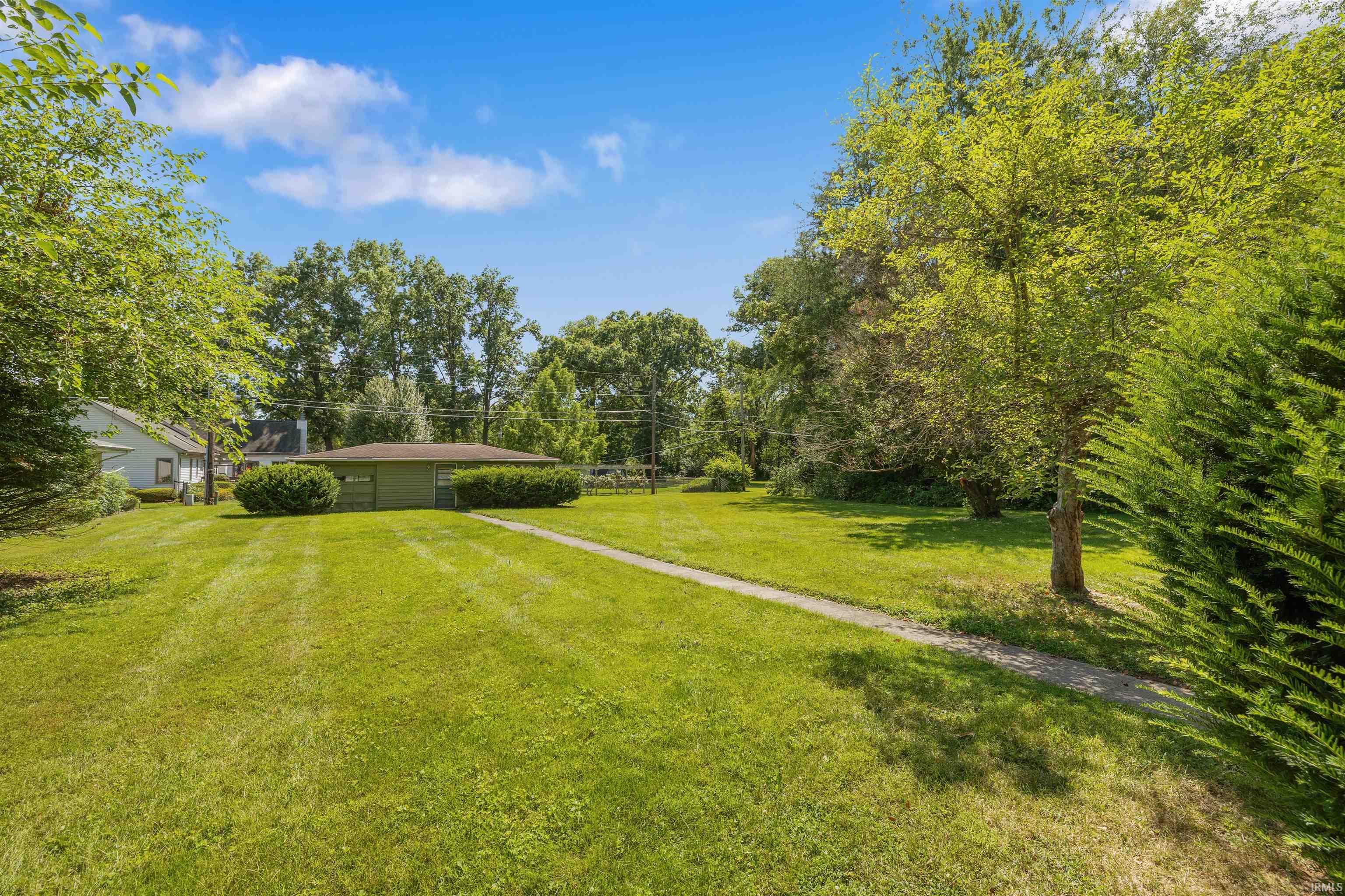 Expansive grounds featuring a manicured lawn with mature trees lining the perimeter, a long driveway approach, and a single-story residence set back on the property