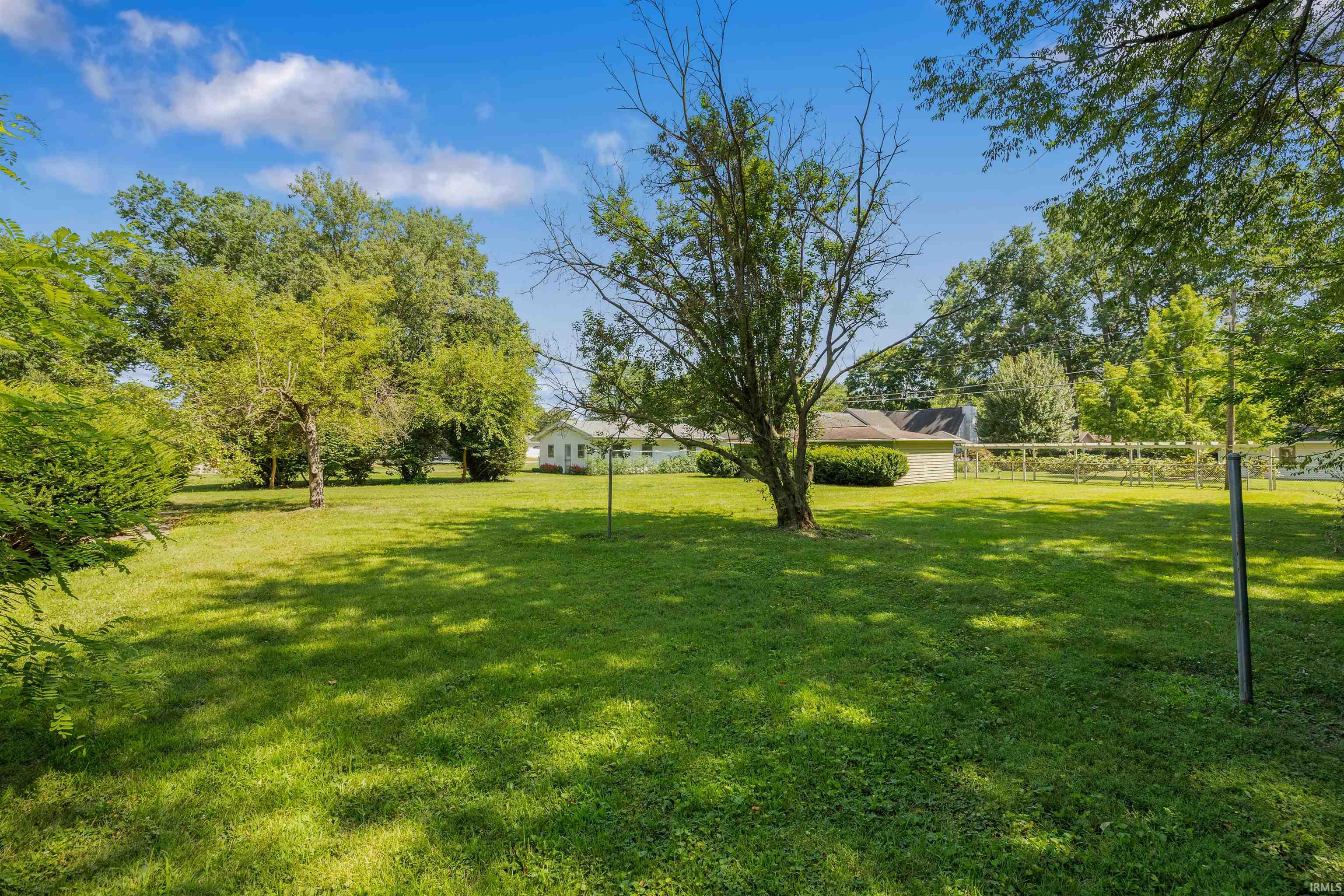 Expansive grounds featuring a manicured lawn with mature trees, wooden fencing, and open pasture space