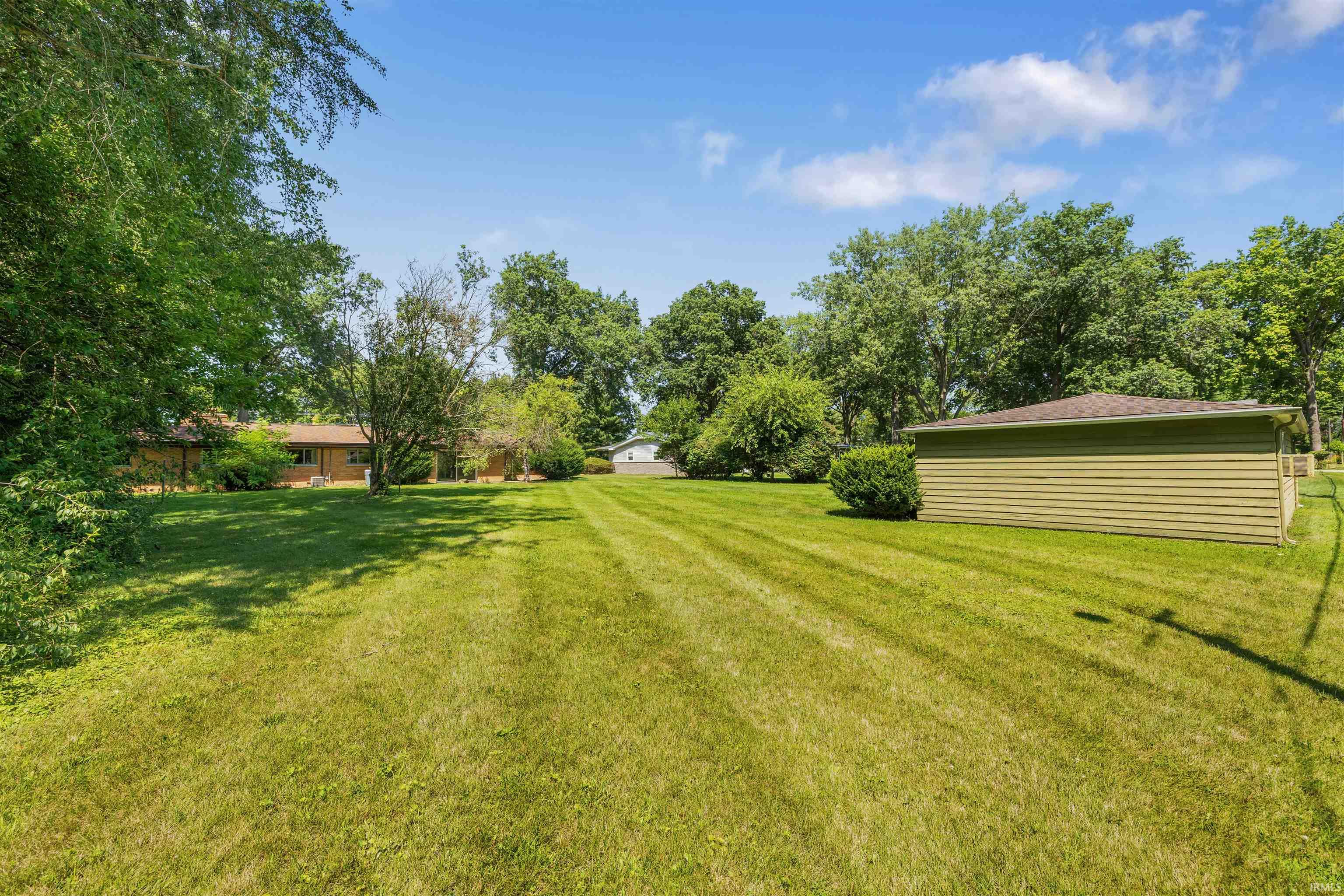 Expansive green lawn with mature trees and a detached outbuilding featuring horizontal siding and a shingle roof