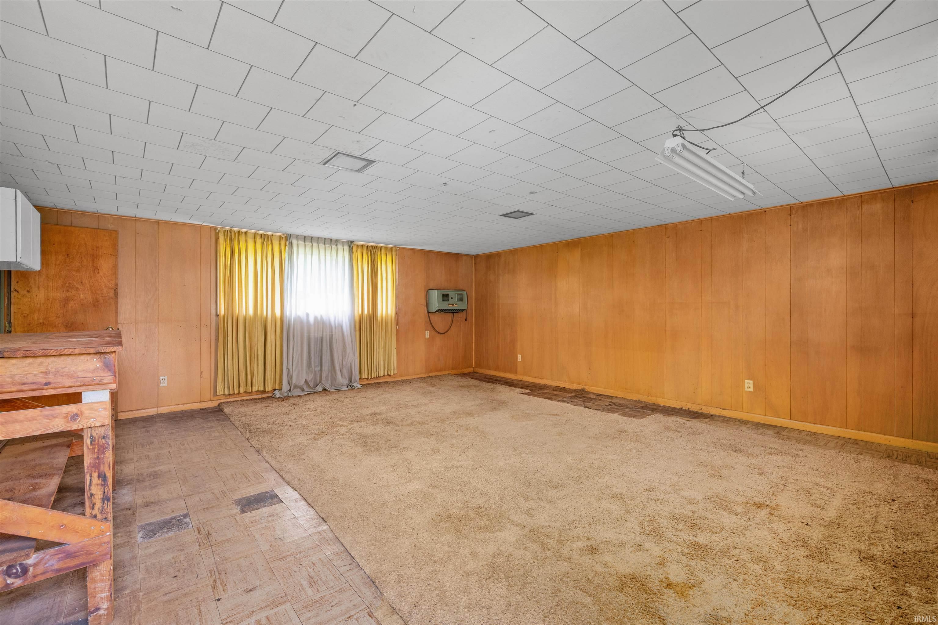 Spacious room featuring wood paneling, drop ceiling, and carpeted flooring