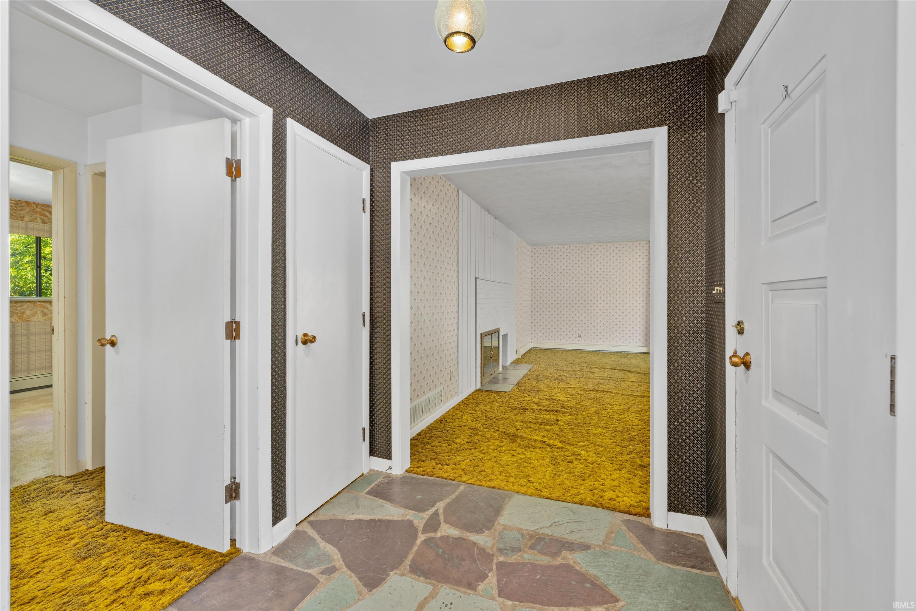 Elegant foyer showcasing multiple white six-panel closet doors with brass hardware, warm wood-finish flooring in the primary space, and geometric patterned area rug