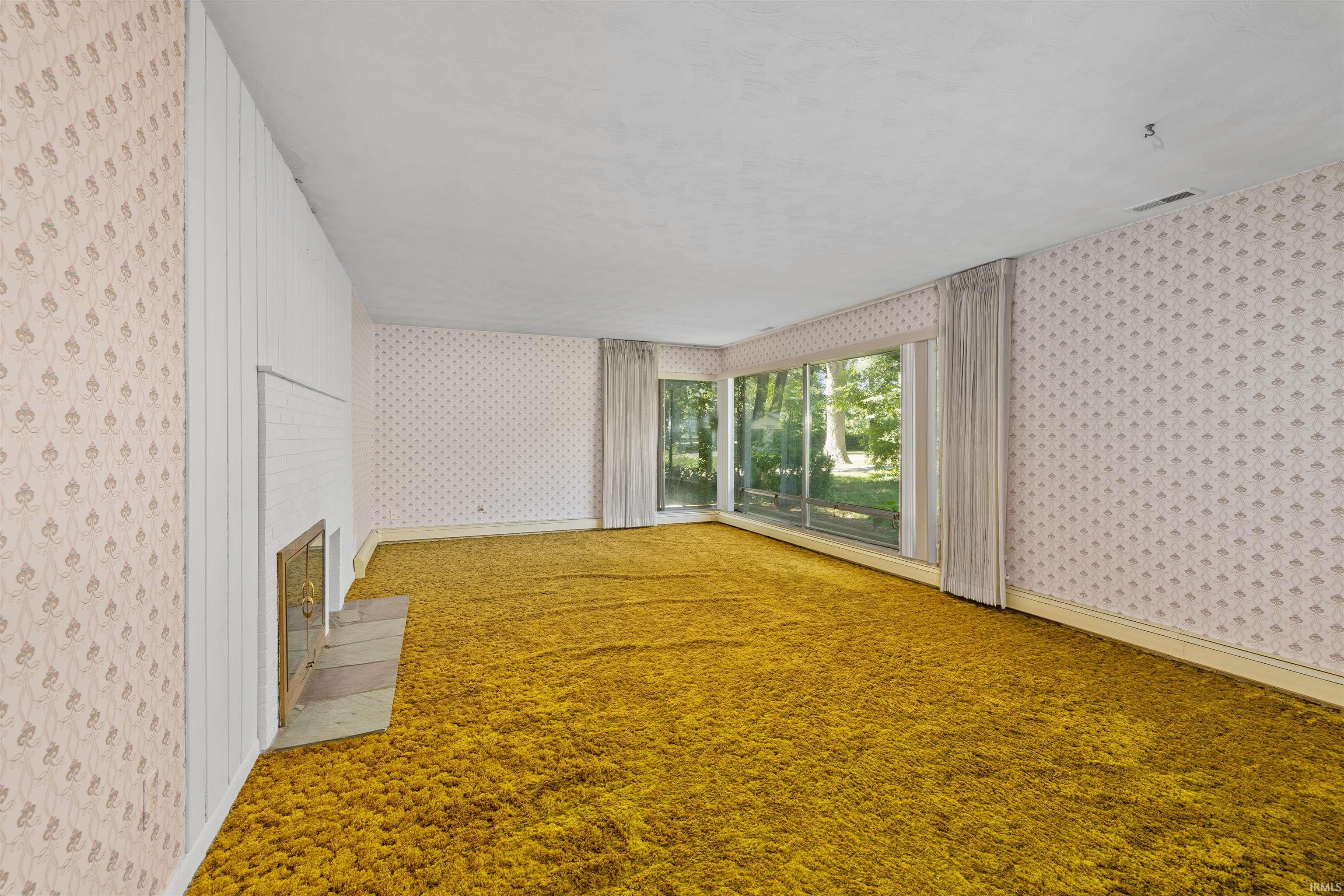 Spacious room featuring golden-toned carpet flooring, soft-patterned wallcovering throughout, and abundant natural light from multi-pane windows with operable glass doors
