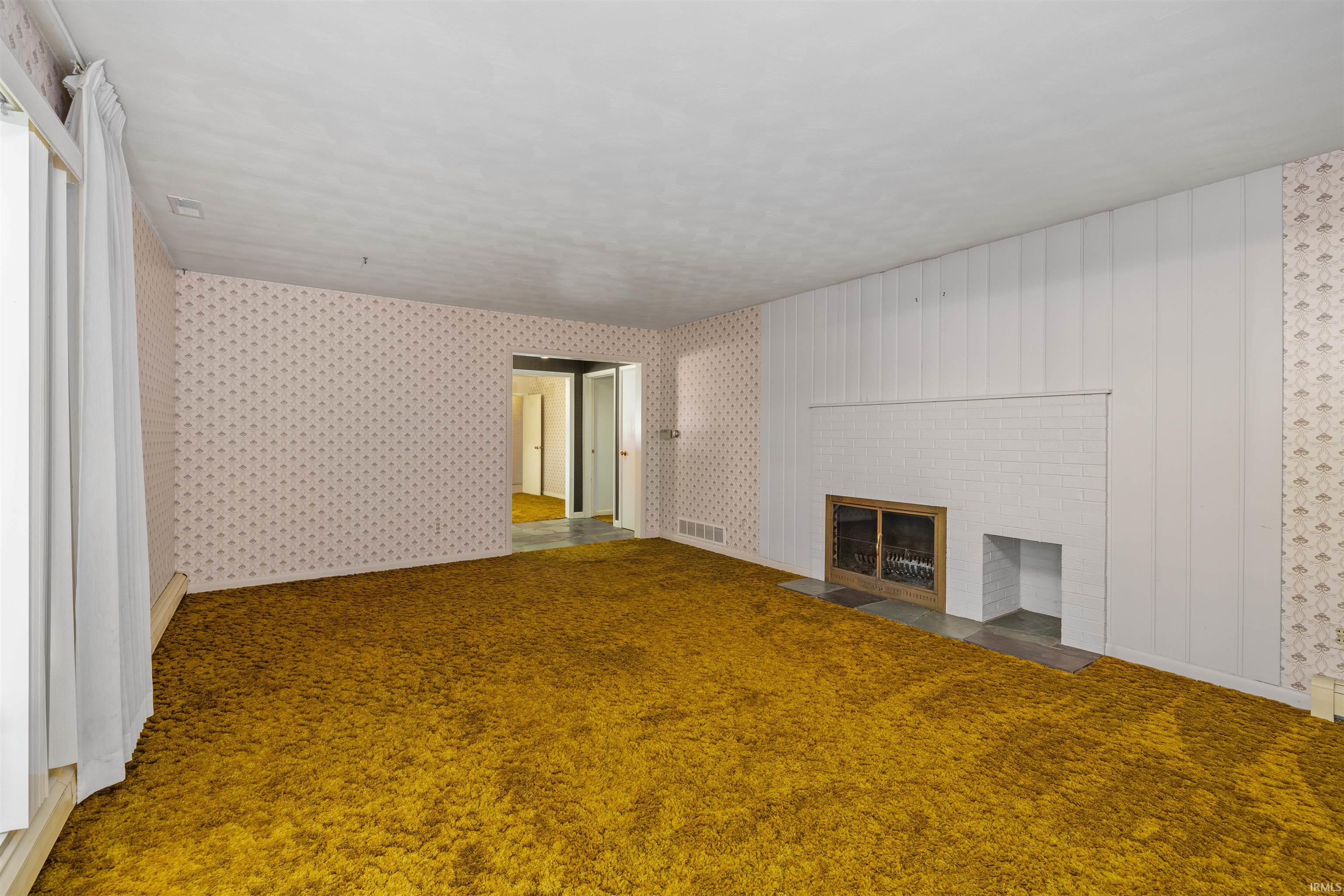 Spacious living area showcasing golden-toned carpet flooring, white vertical shiplap accent wall, and built-in fireplace with integrated shelving