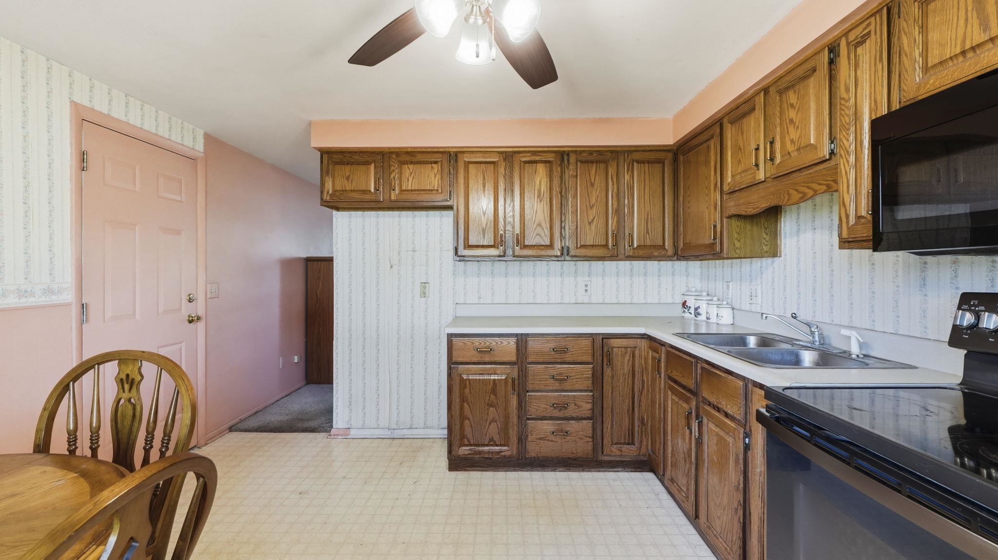 Spacious kitchen featuring wood-finish cabinetry with ample storage, white subway tile backsplash, stainless steel appliances including a black range, and ceramic tile flooring
