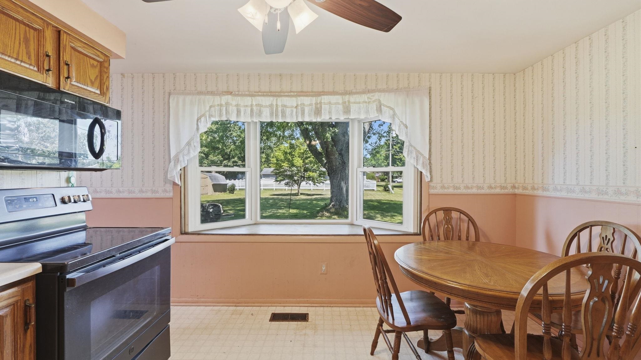Bright dining area with wood-finish flooring, ample natural light from triple glass doors, and expansive views of manicured grounds and mature landscaping
