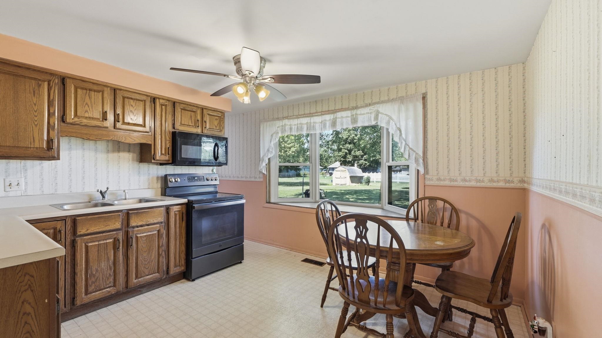 Charming kitchen and dining area featuring wood cabinetry with traditional styling, black electric range, tile flooring, and a ceiling fan with integrated lighting