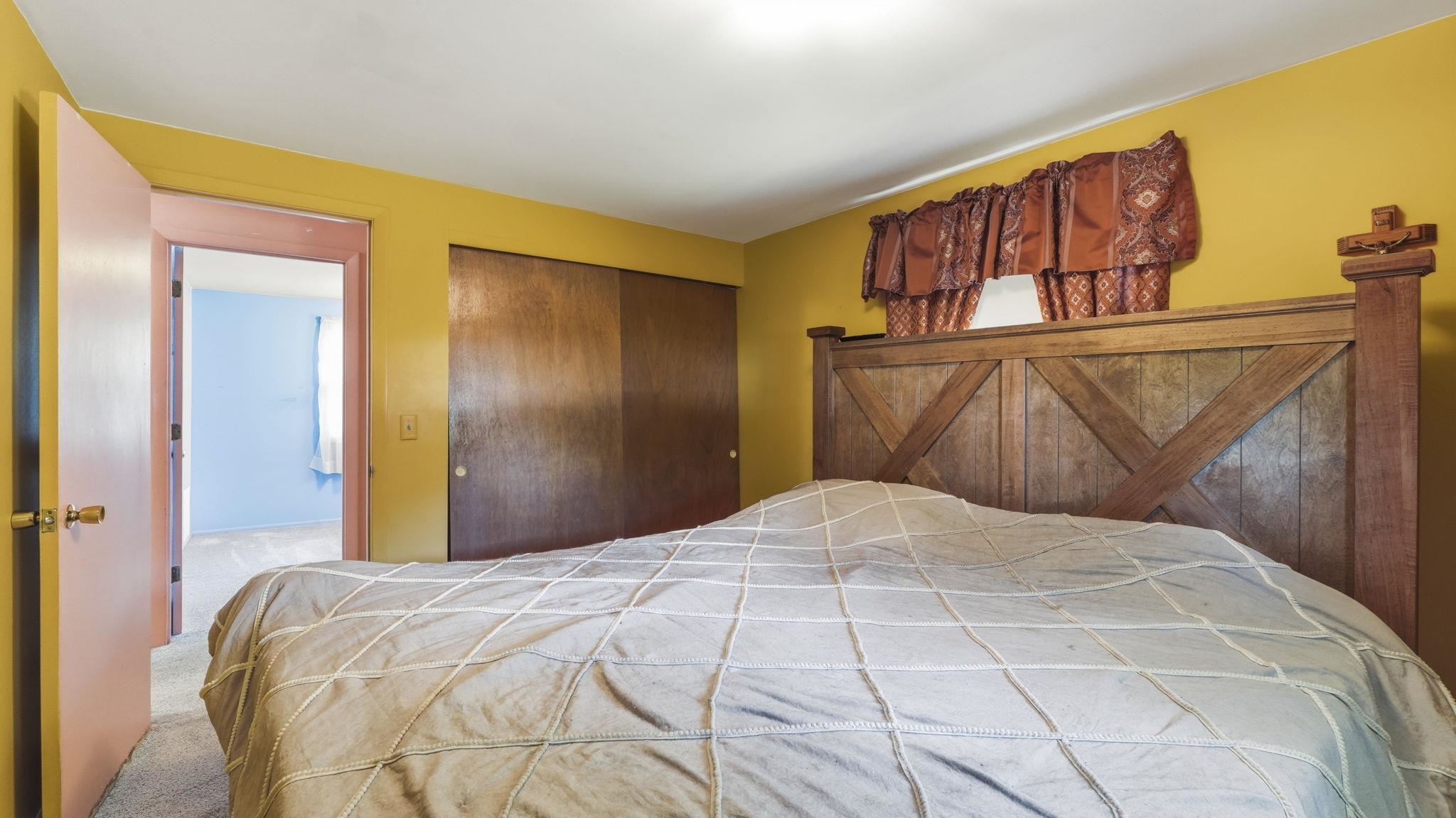 Spacious bedroom featuring warm yellow walls, wood-finish barn-style headboard with X-detailing, and dual wood-finish closets with X-panel doors