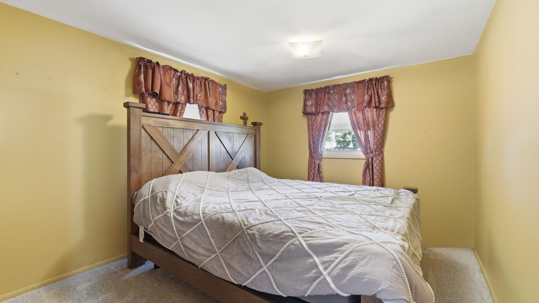 Charming bedroom showcasing warm yellow walls, a wood-frame bed with X-pattern detailing, and burgundy window treatments