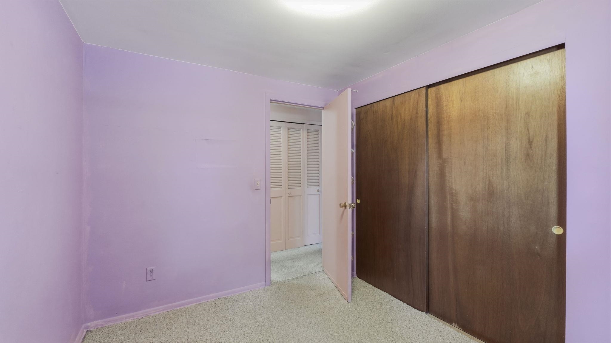 Bedroom featuring light purple walls, a ceiling-mounted light fixture, light-toned carpeting, and a closet with wood-finish sliding doors