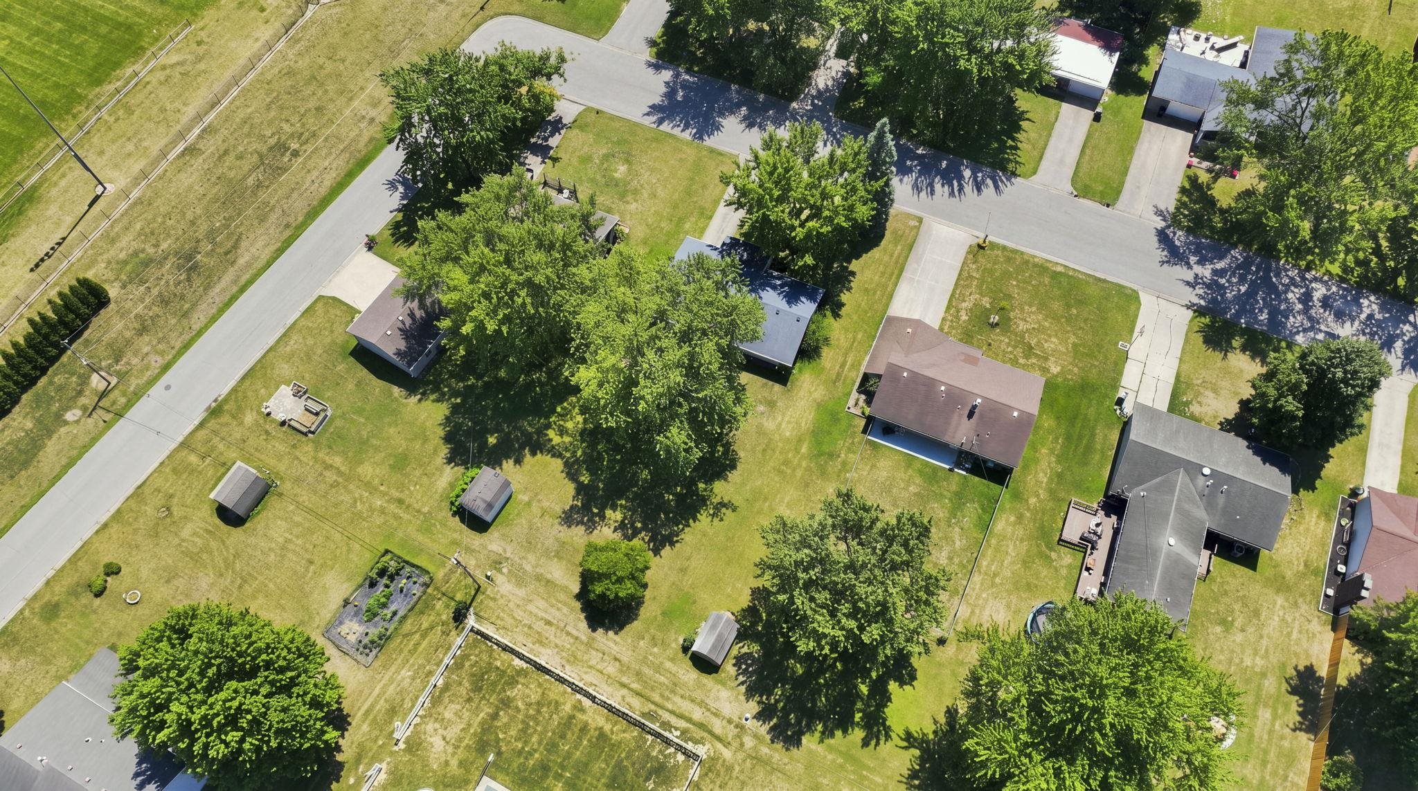 Aerial view showcasing expansive residential lot with mature shade trees, established landscaping, and multiple outbuildings