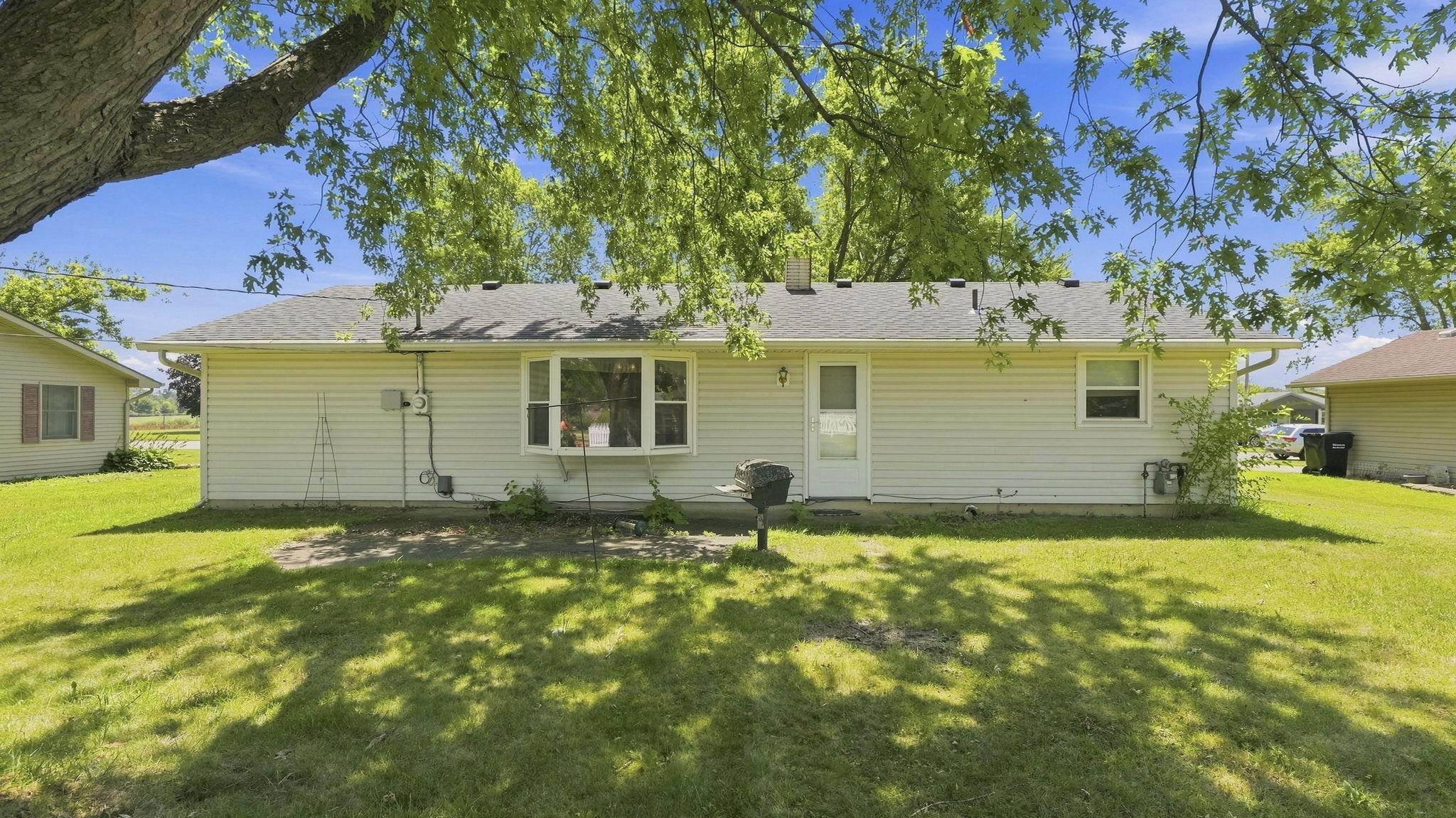 Charming ranch-style home with vinyl siding and a welcoming front entrance, situated on a spacious lawn shaded by mature trees