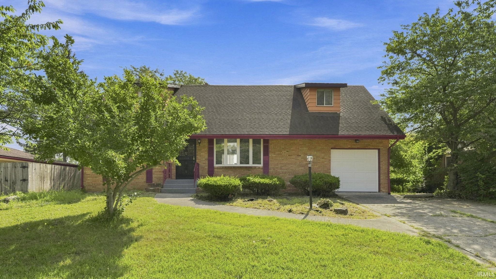 Brick-clad residence featuring a single-car garage, dormer window, and mature front yard tree