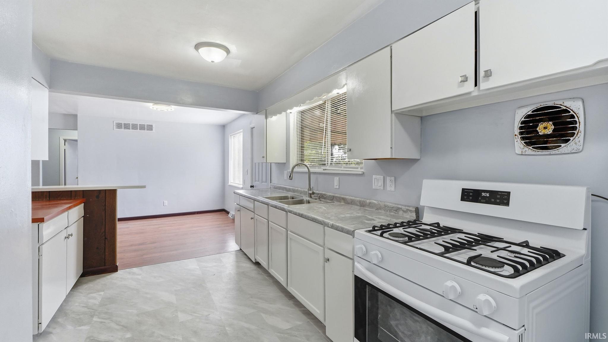 Kitchen featuring white cabinetry, a dual basin sink, a gas range, and light-toned flooring